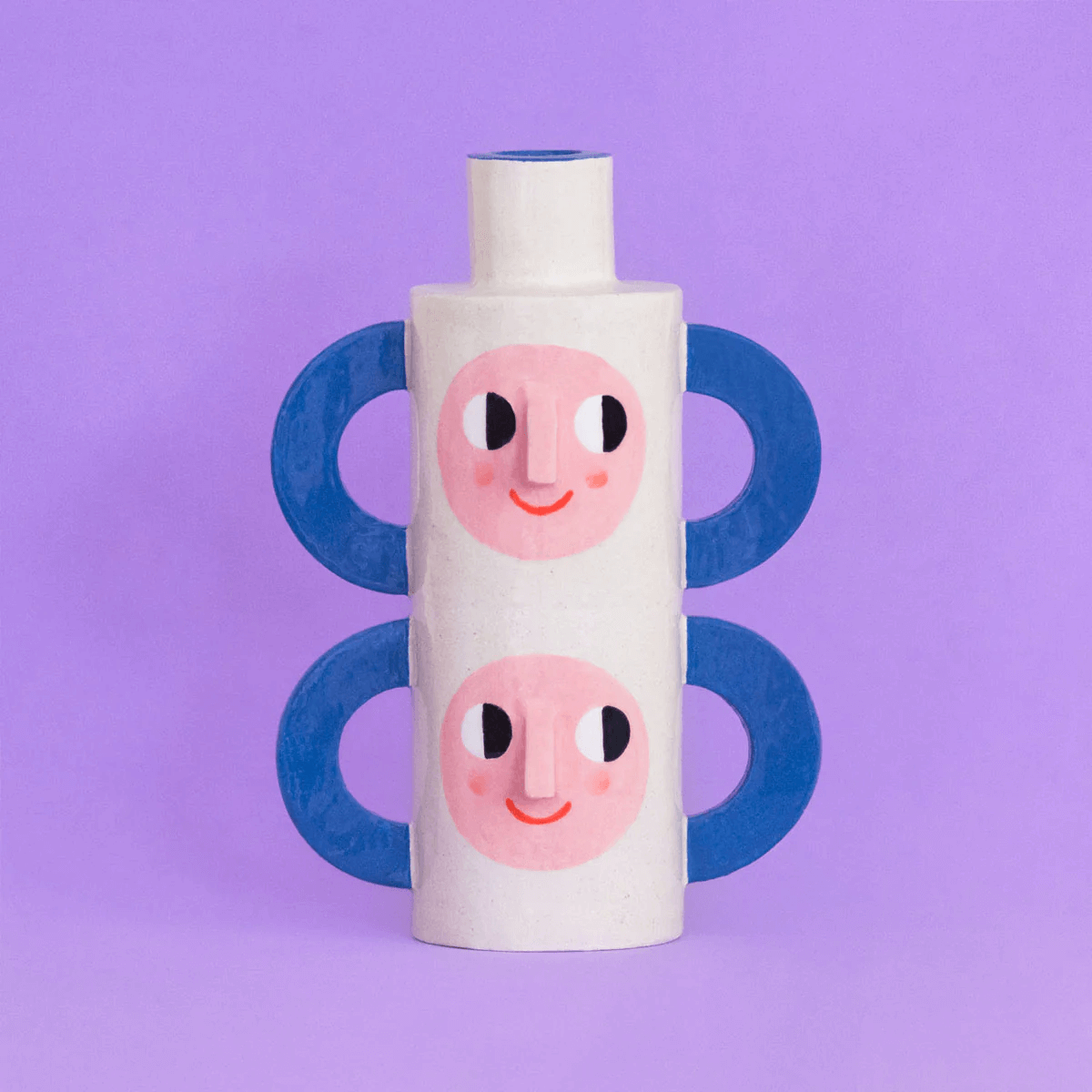 Tazas blancas con caras sonrientes, con mangos azules, colocadas una encima de otra sobre fondo lila.