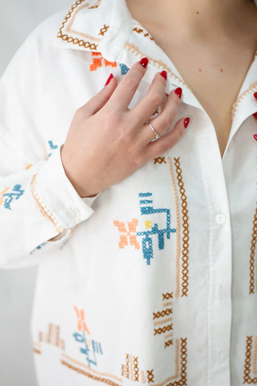 Parte superior de un vestido sin mangas de color blanco con bordados de flores en tonos naranja, rosa, azul y verde, y botones en la parte frontal.