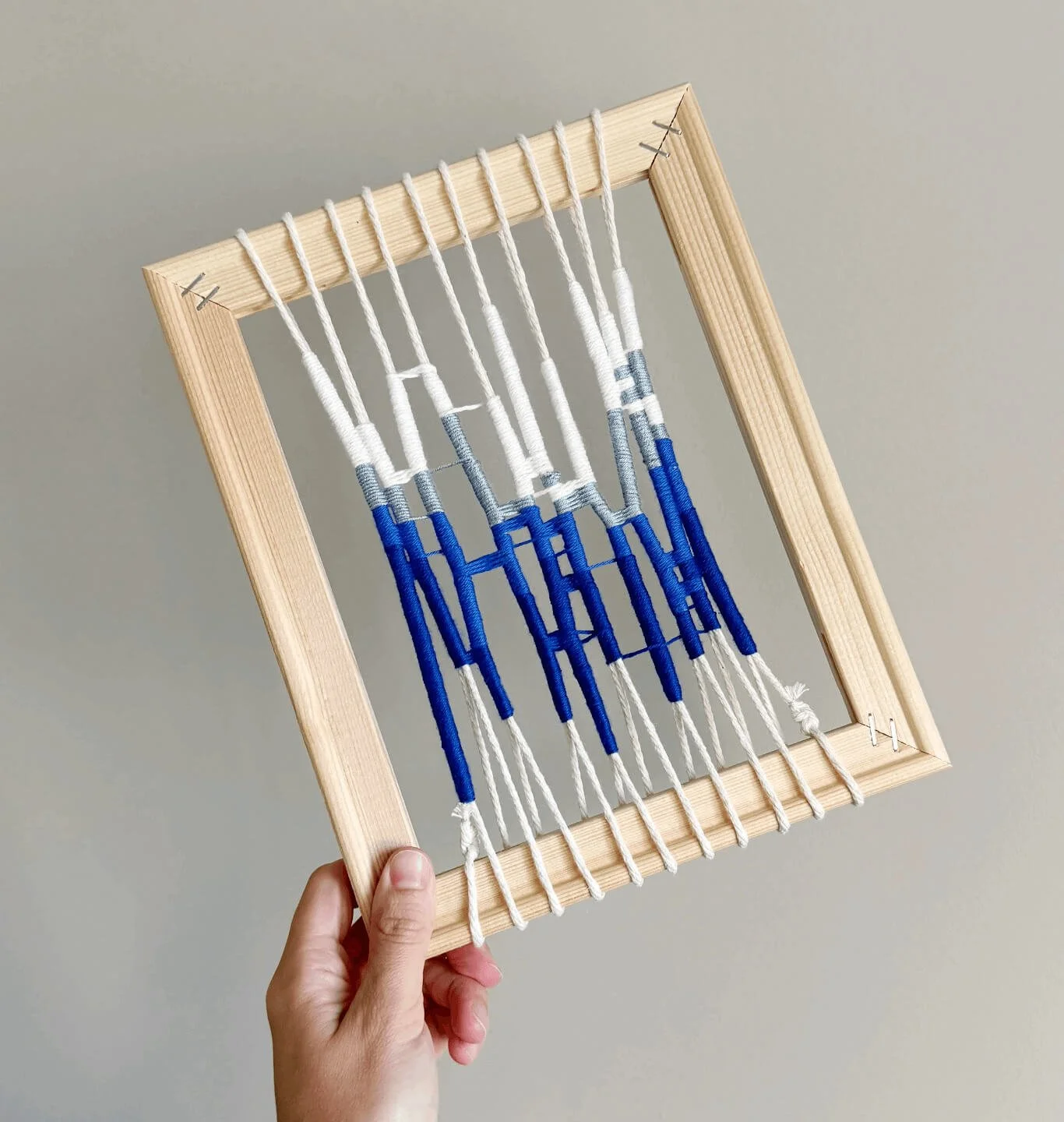 Marco de madera con hilos de bordar con bordado en azul y gris.