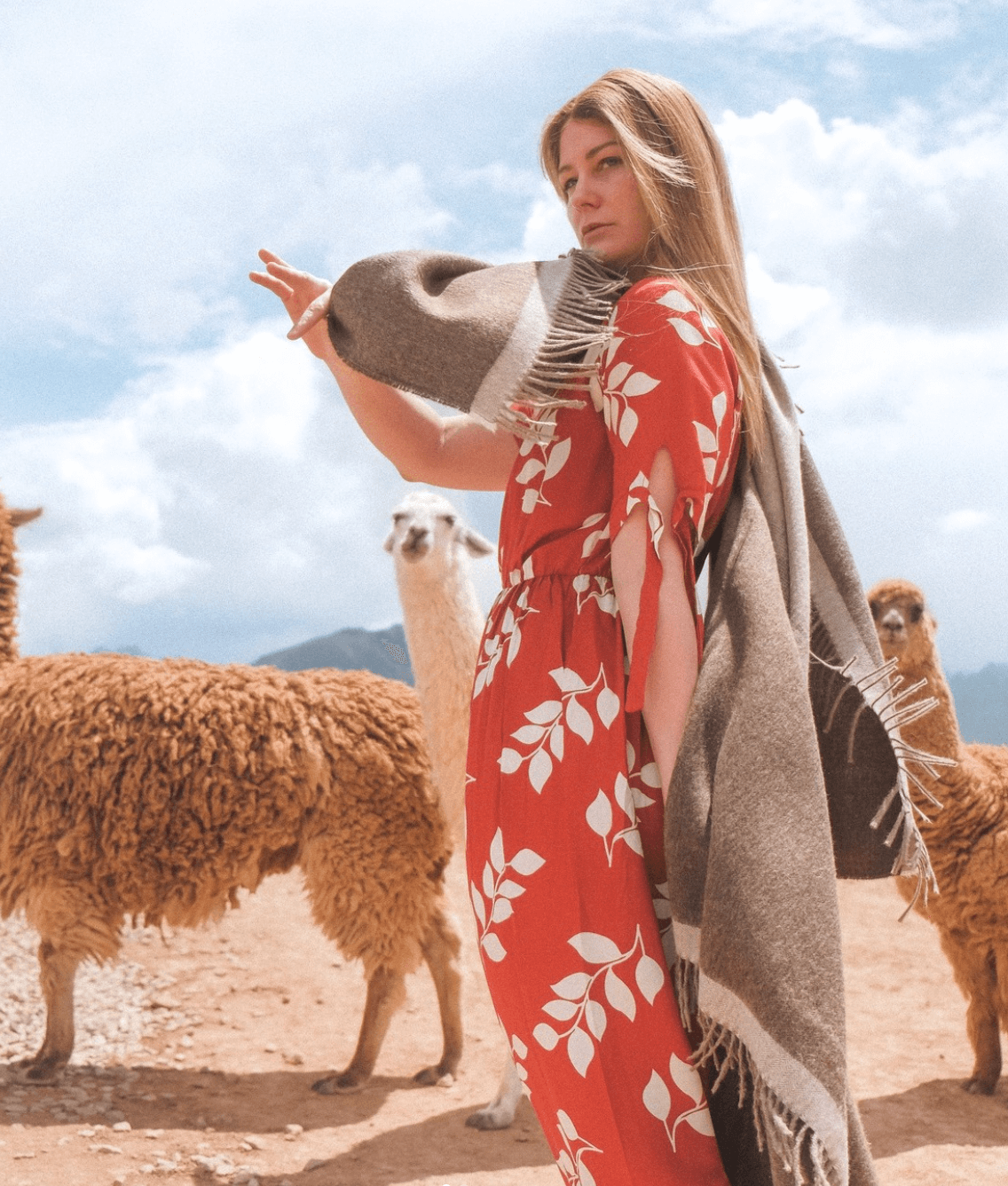 Mujer con vestido rojo y bufanda en un campo con ovejas bajo cielo azul