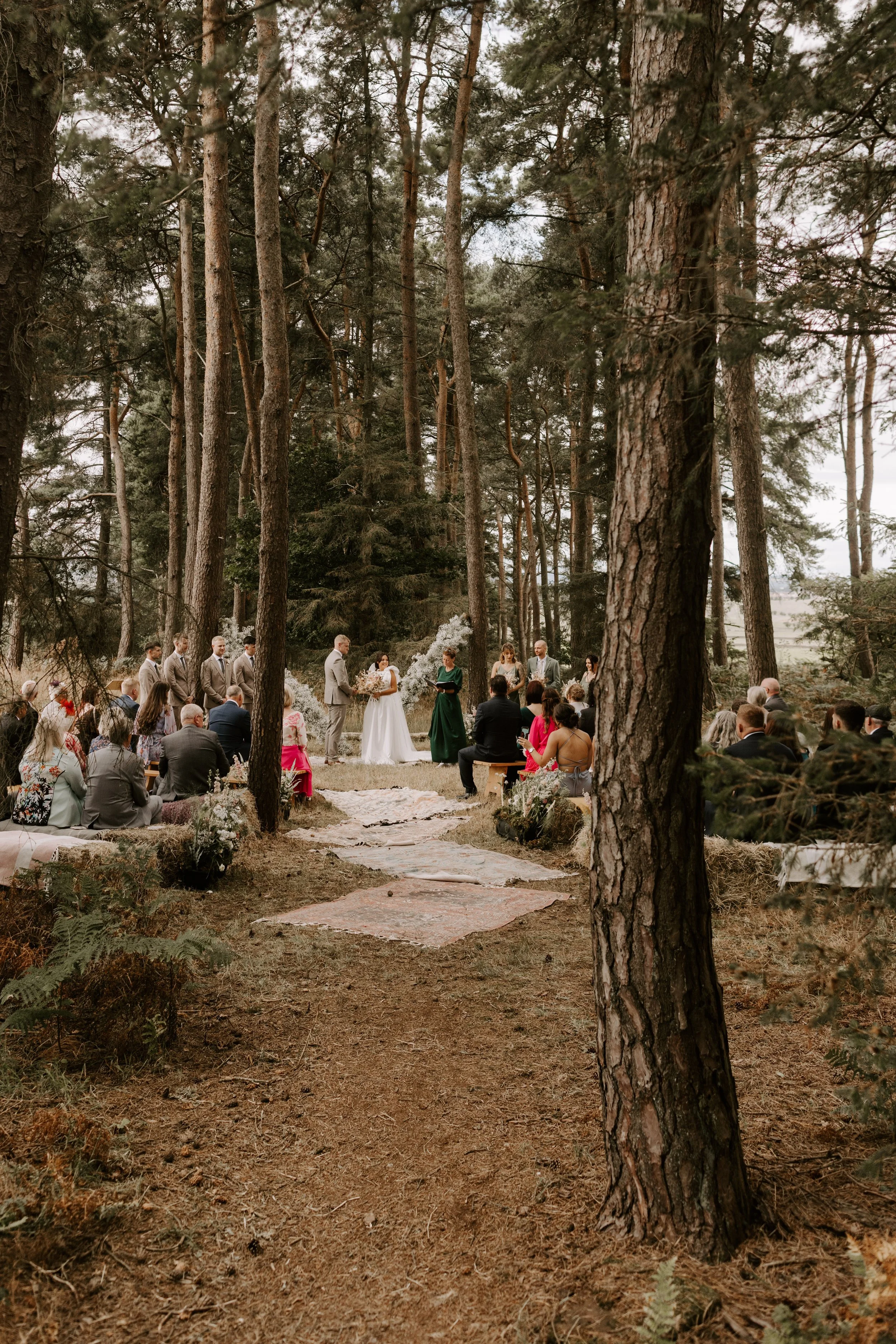 Outdoor wedding ceremony in a forest setting with guests seated and a couple standing together.