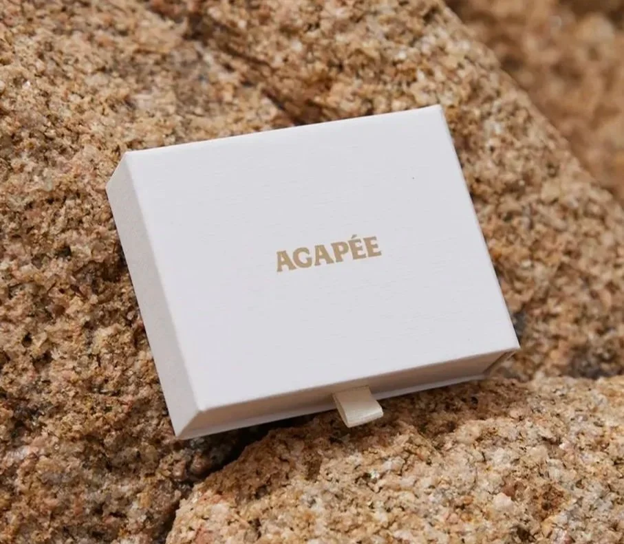 Small white box with gold text that says 'AGAPÉ,' resting on rocks.