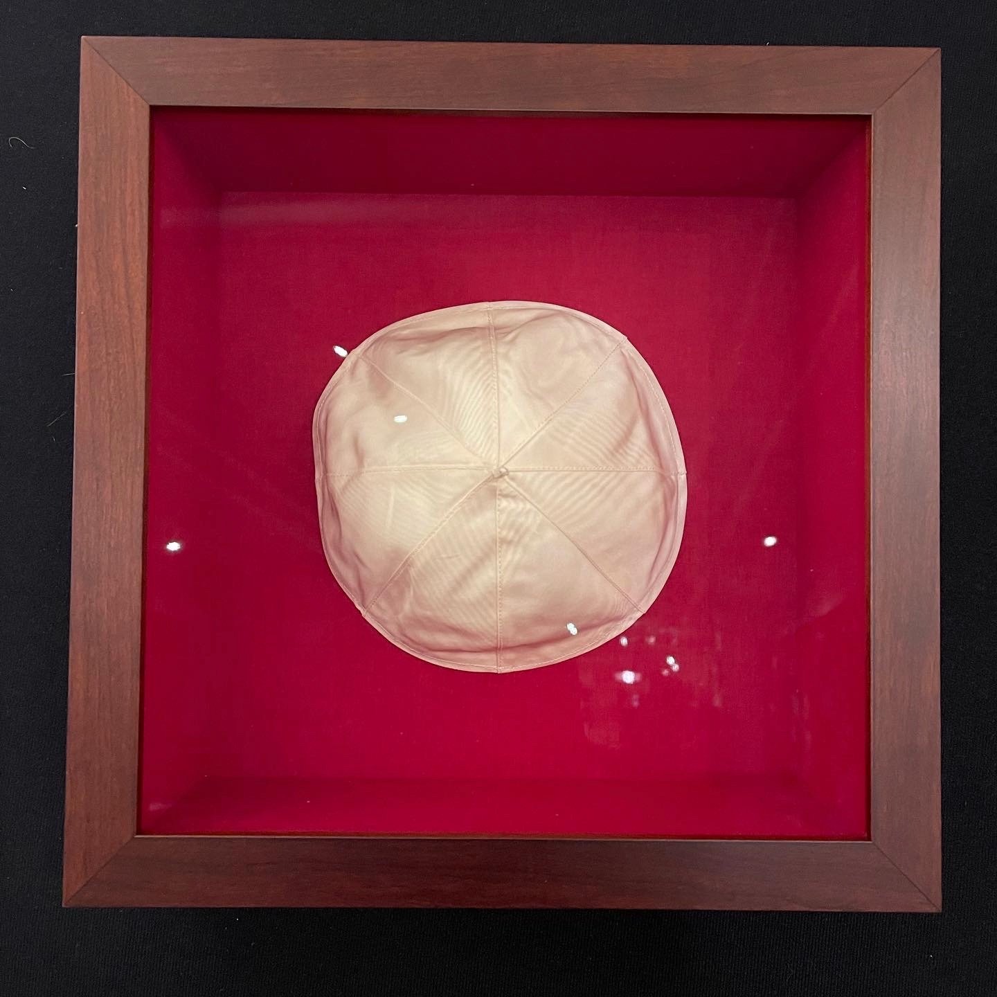 Deep wooden shadow box lined with red fabric to display a white satin zucchetto