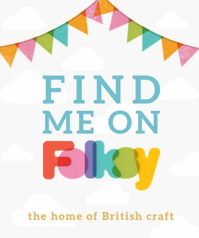 Colourful bunting flags hanging above, with the text "Find Me on Folksy" and a subtitle "the home of British craft" against a light background with clouds.
