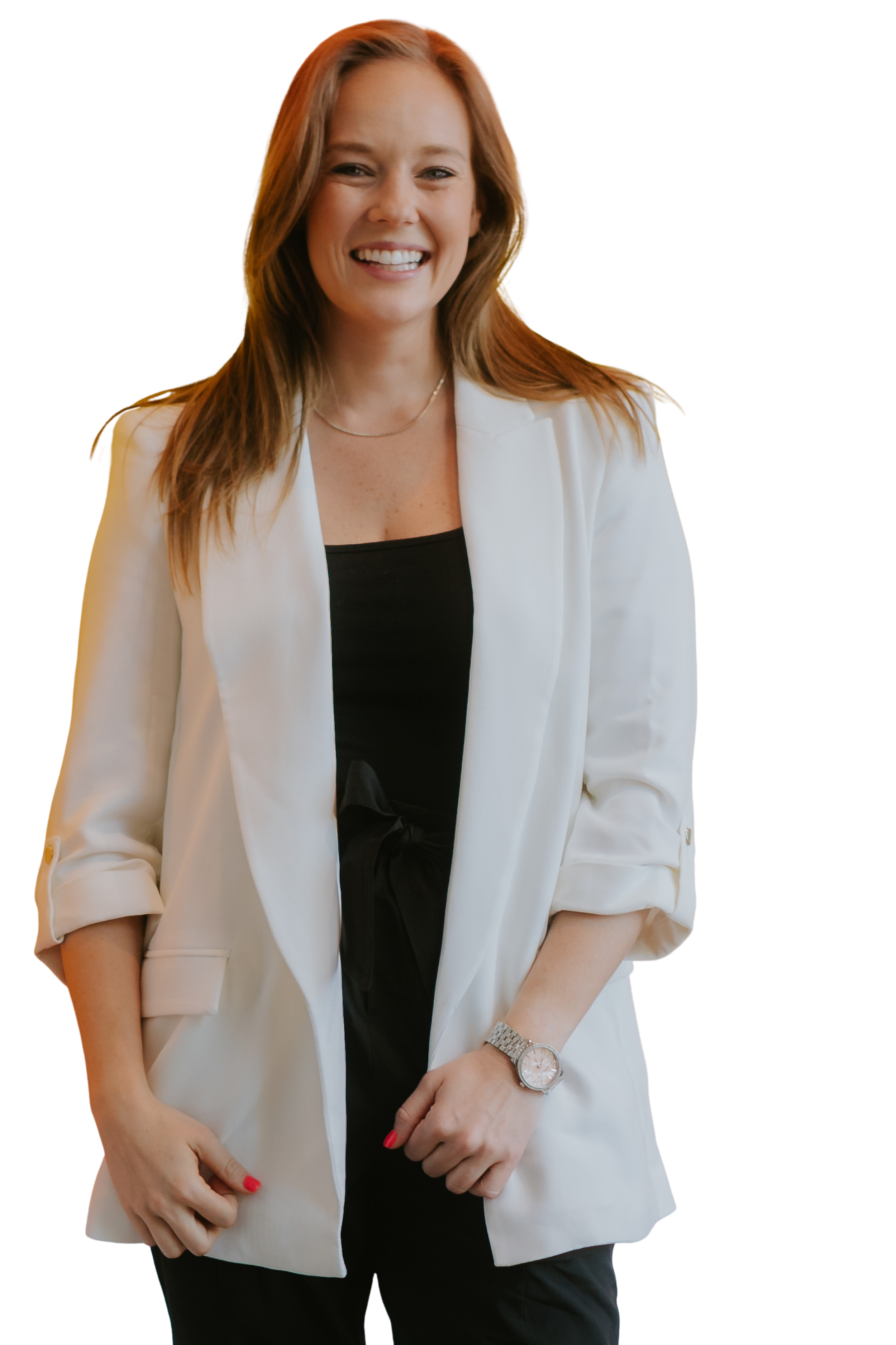 A woman with long reddish-brown hair, smiling, dressed in a black top and white blazer, wearing a wristwatch and red nail polish, standing with her hands clasped in front of her.