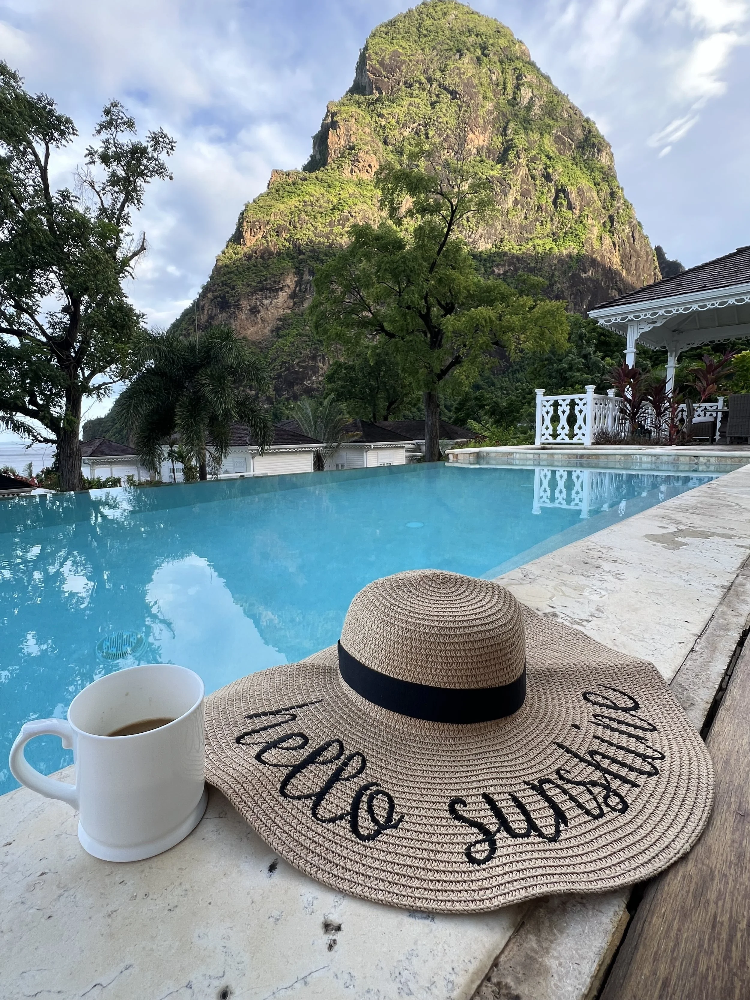 hello sunshine hat and a cup of coffee on the edge of a plunge pool with the pitons in the background