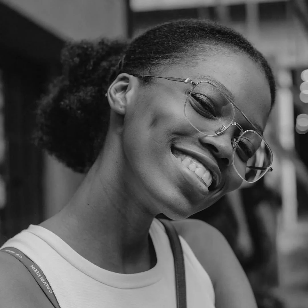 A smiling woman with glasses and braided hair, wearing a sleeveless top.