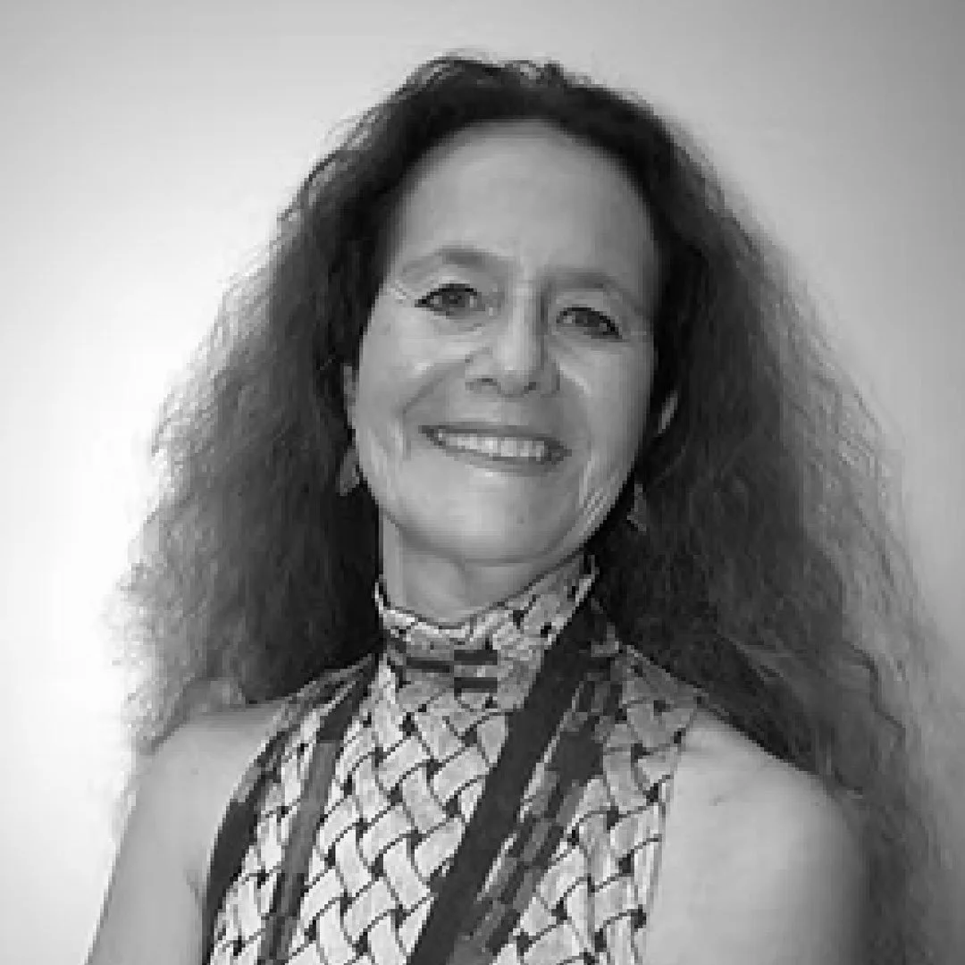 Black and white portrait of a woman smiling with long curly hair, wearing a patterned top with a high collar.