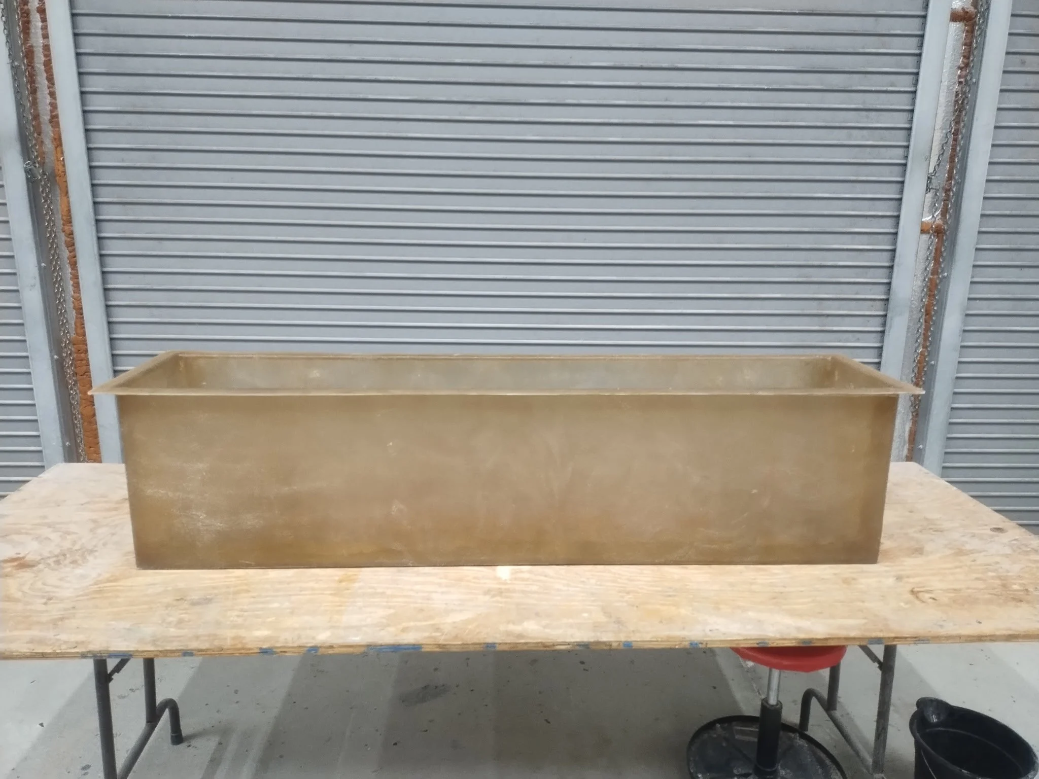 A large metal container on a wooden work surface in front of a metal roll-up door.