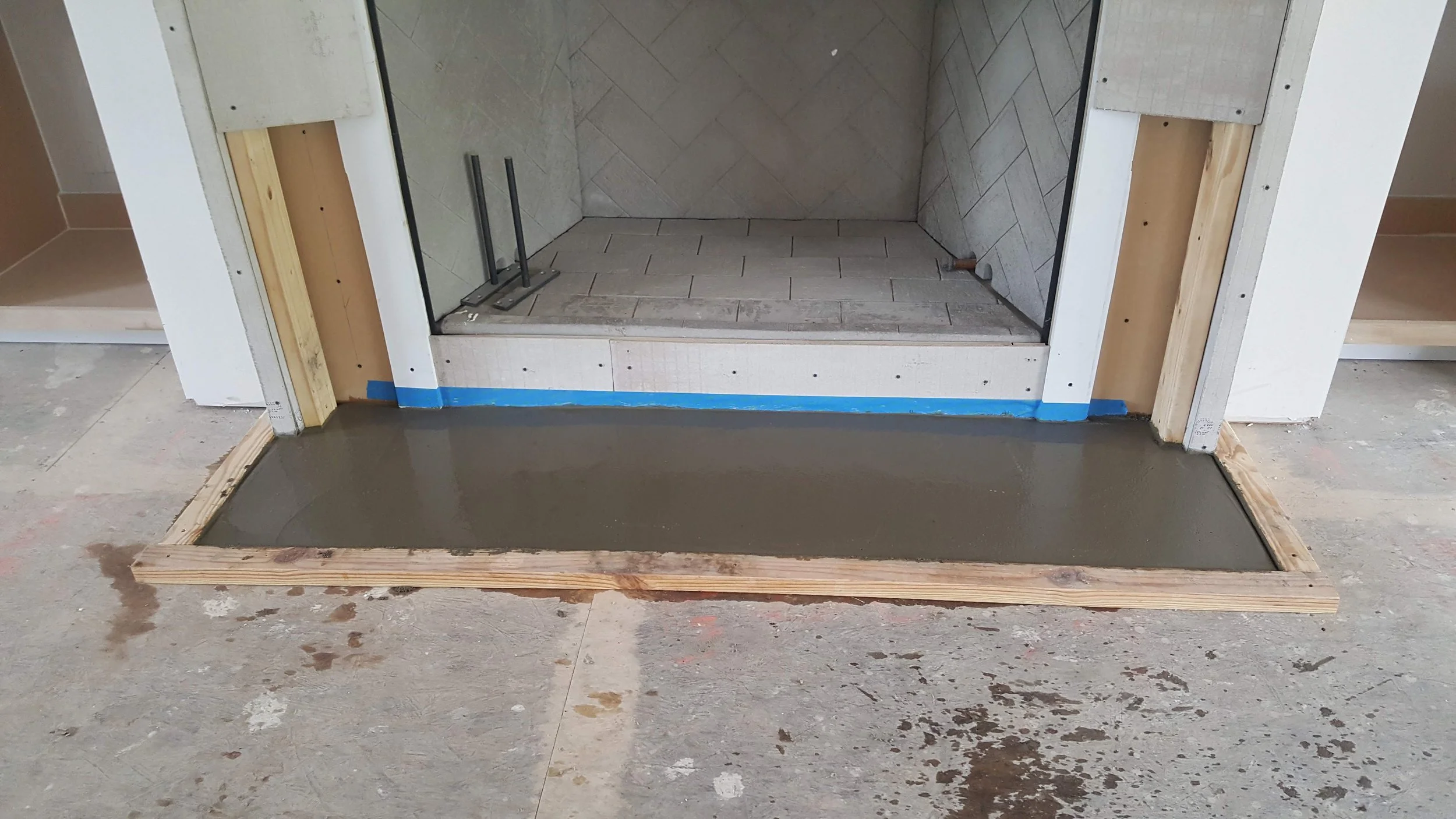 Unfinished fireplace with concrete slab in front, framing for a hearth, and interior with tile walls.