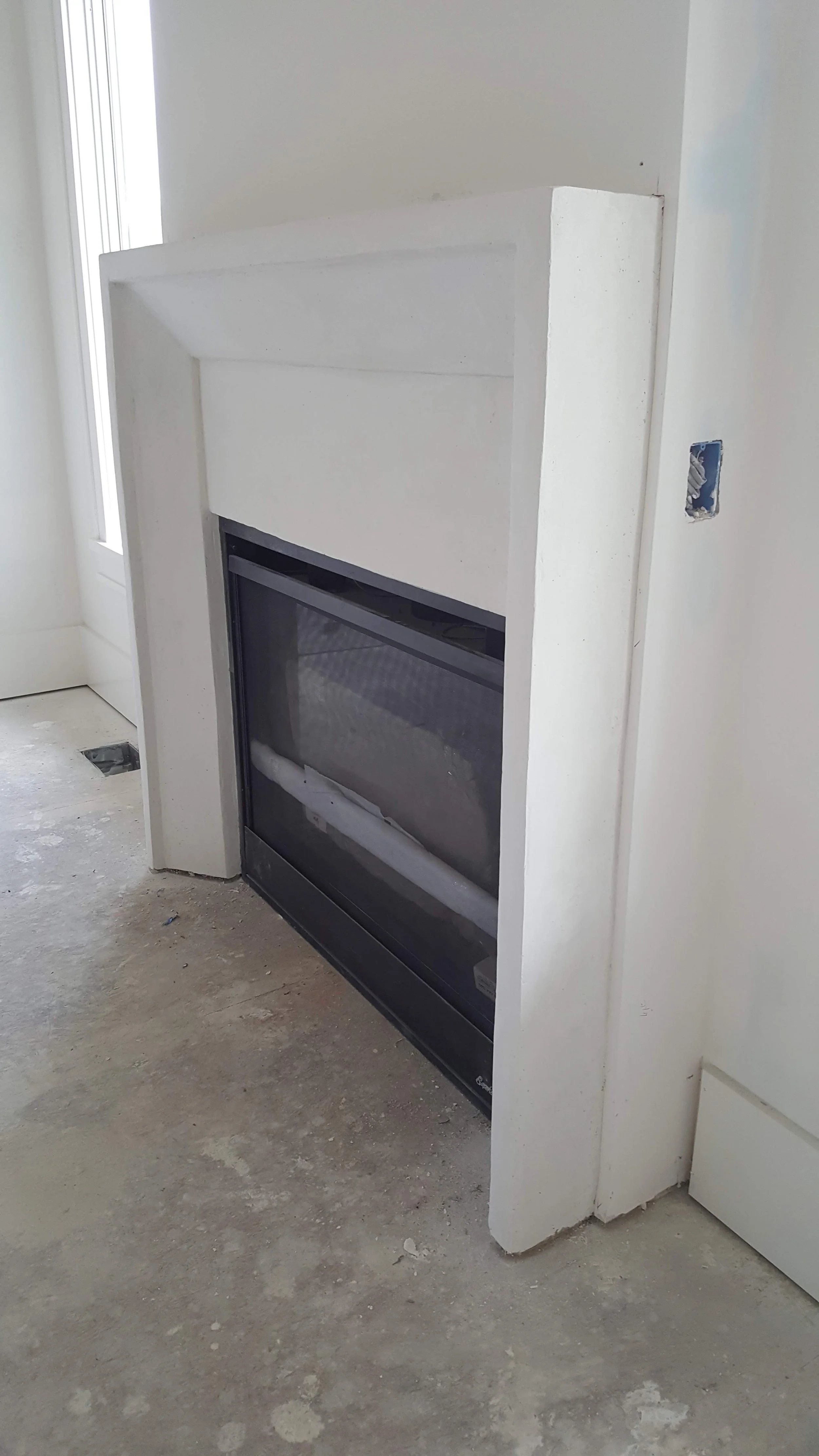 Unfinished fireplace with a black glass door and white framing in a room under renovation.