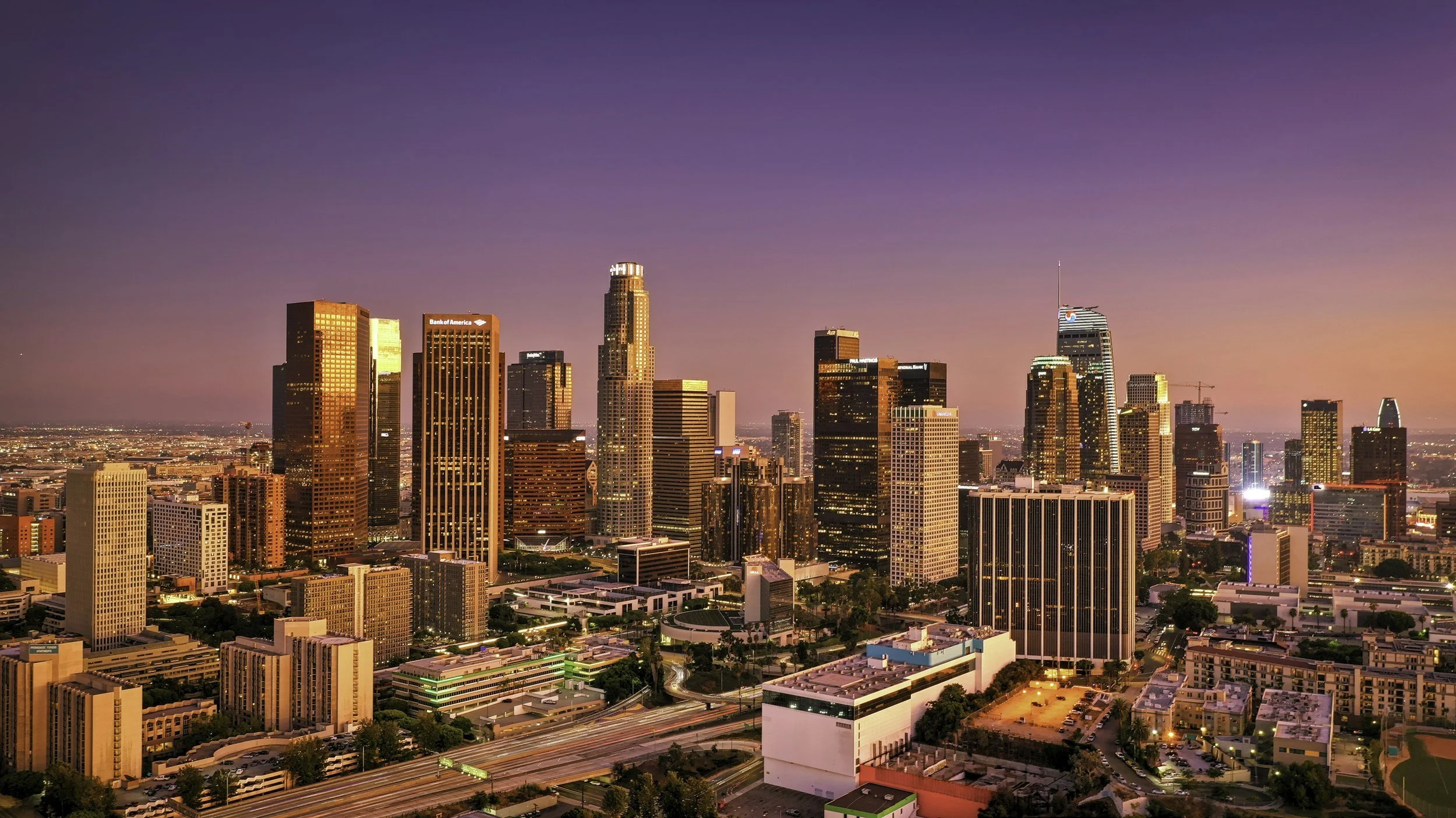 Street scene in Hollywood, Los Angeles, with palm trees lining the street, neon signs, and bustling traffic at sunset.