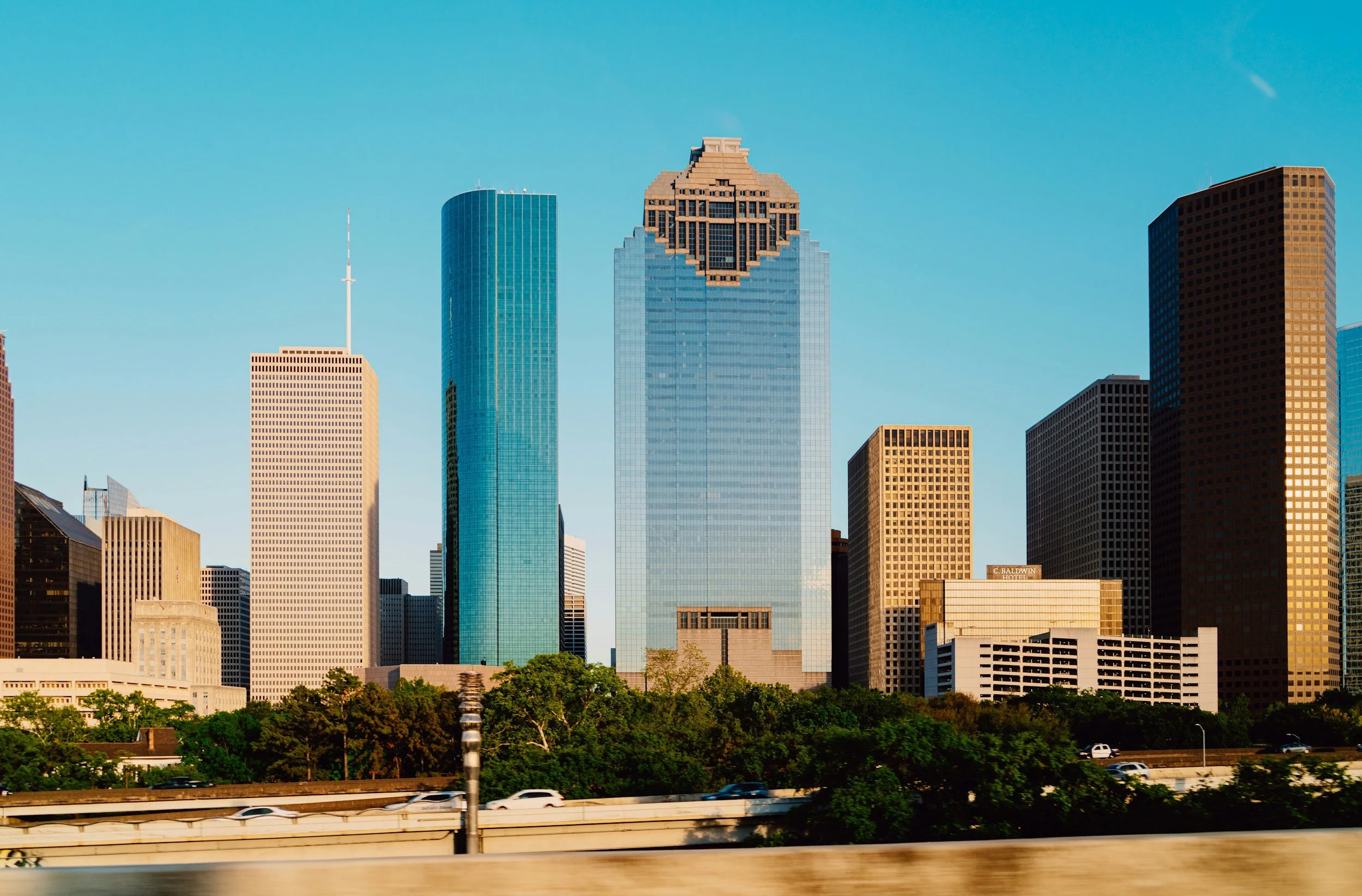 Houston, Texas skyline at sunset with skyscrapers, a river, and a bridge crossing over the water.