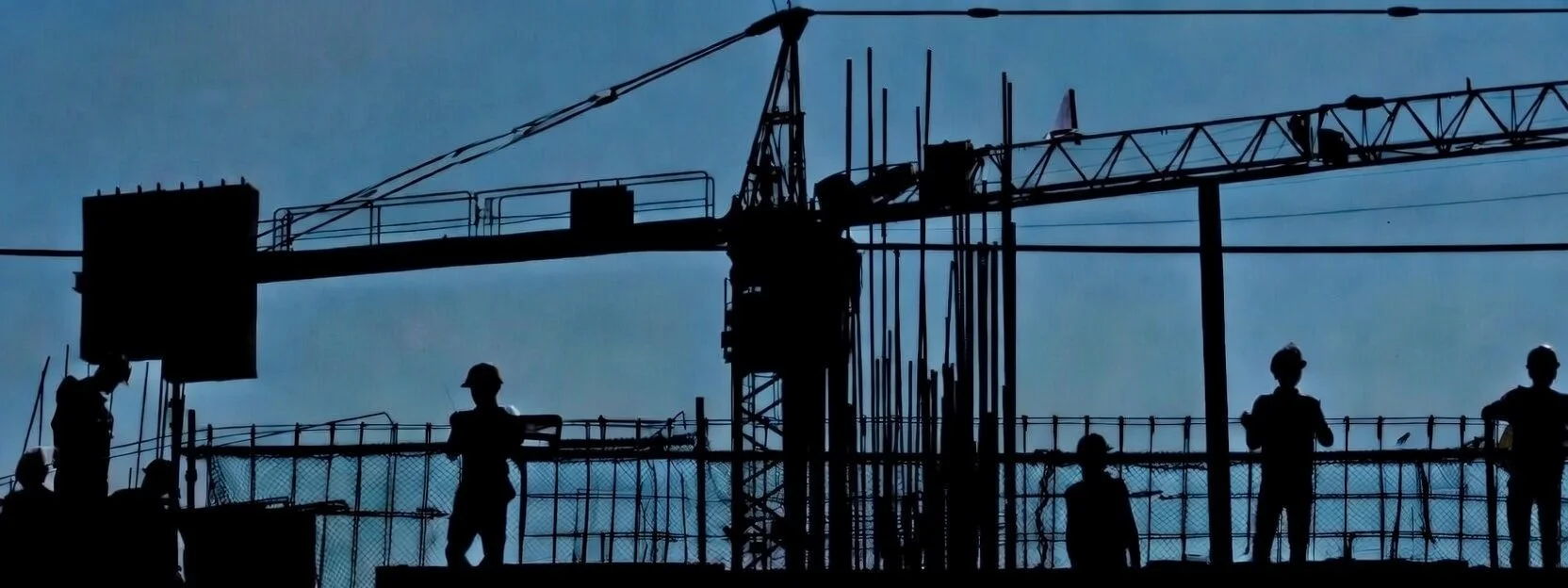 Silhouettes of construction workers standing on a building site, with a crane in the background against a blue sky.