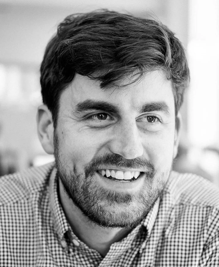 Black and white portrait of a man with dark hair, dressed in a suit, resting his chin on his hand, looking upward.