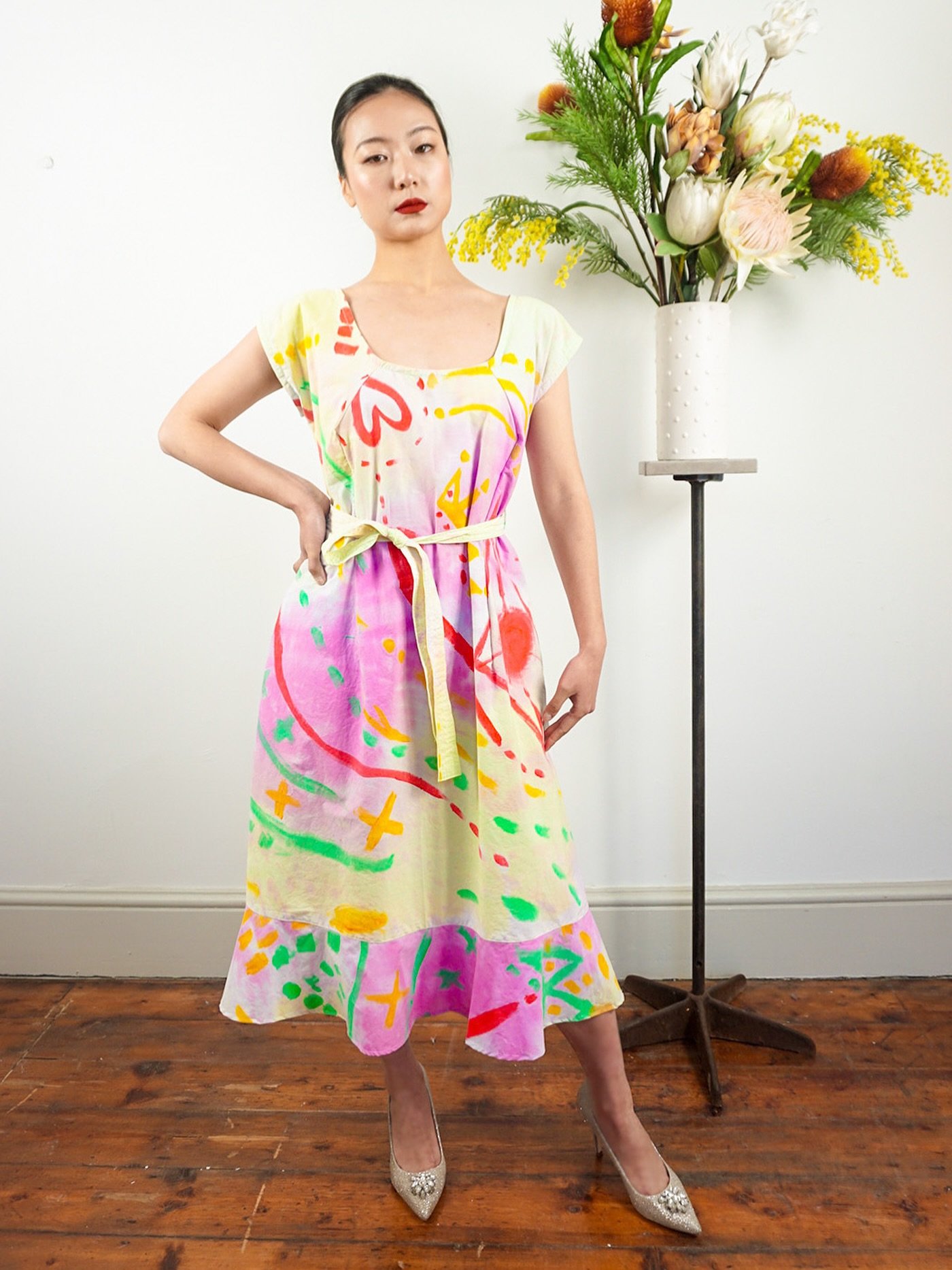 Bring colour and creativity into your wardrobe with this unique cotton midi dress. Featuring a vibrant hand-painted abstract design with splashes of red, pink, yellow, and green on a soft cream base, this dress radiates playful elegance. It has a rel
