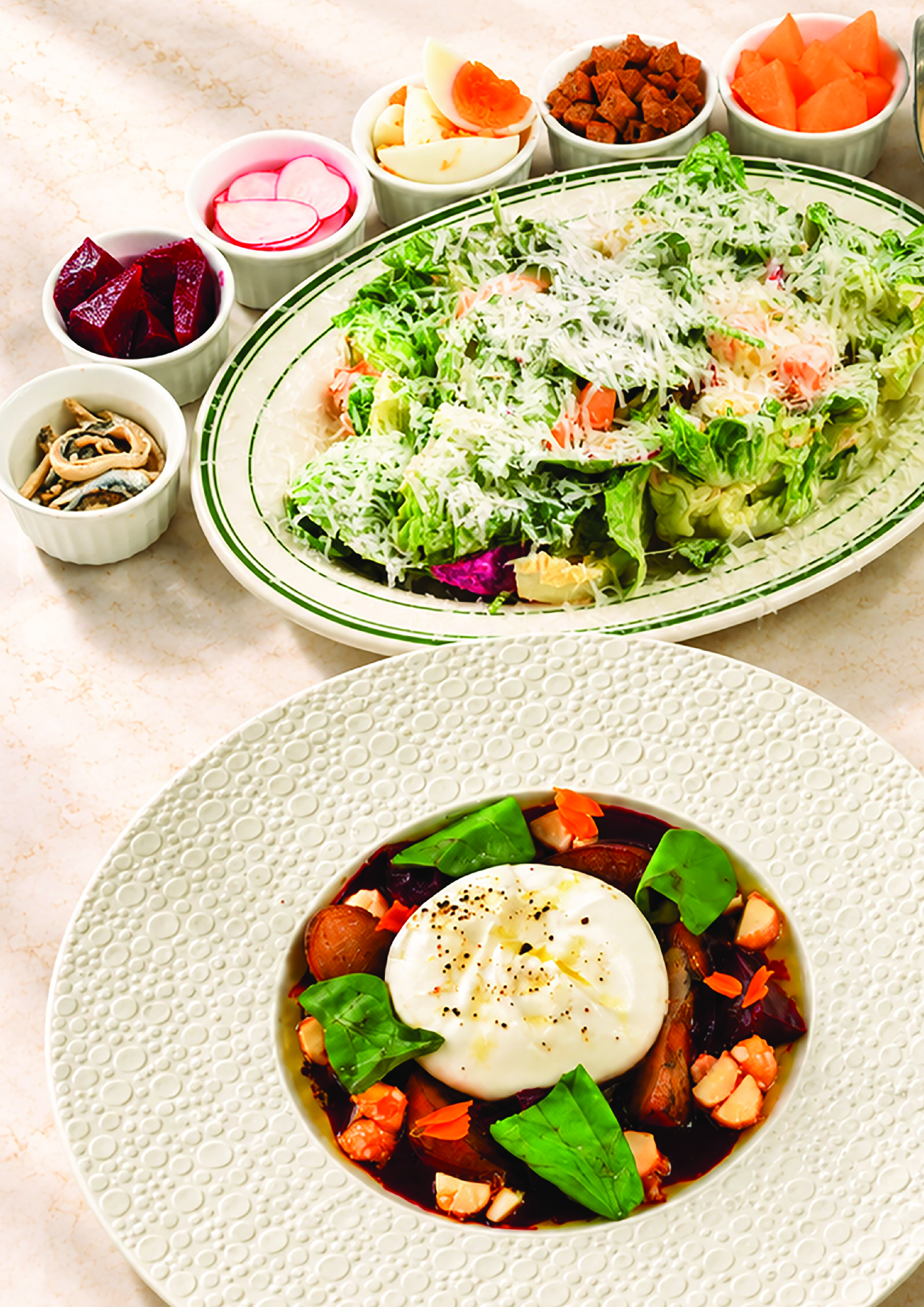 A bowl of huevos divorciados topped with a poached egg, surrounded by chopped vegetables and greens, and a variety of small bowls with pickled vegetables, boiled eggs, chorizo, and fruit.
