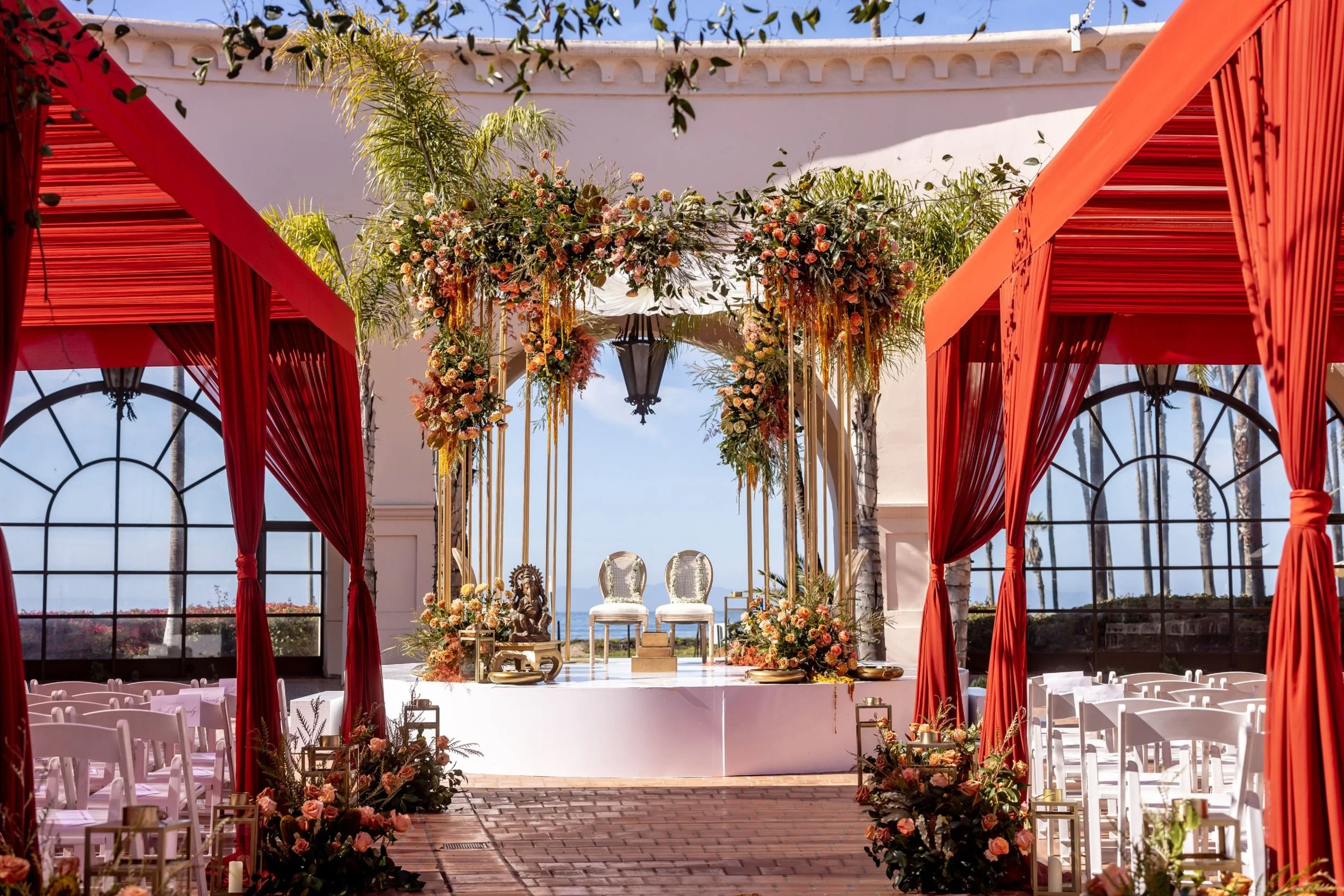 Floral wedding ceremony setting with red drapery and ocean views at Hilton Santa Barbara Beachfront Resort
