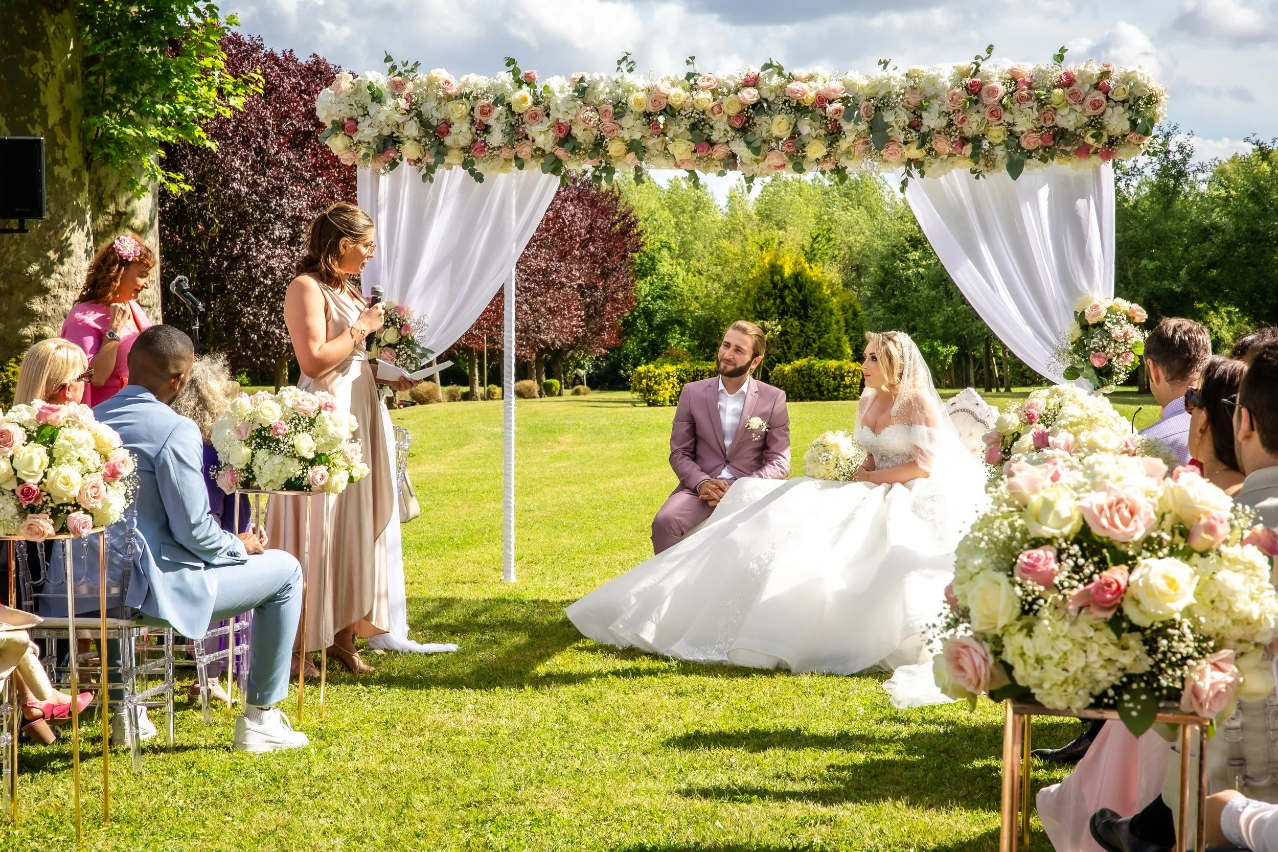 Cérémonie de mariage en extérieur au Château d’Aveny dans le Vexin, sous une arche florale élégante, avec discours émouvant devant les mariés – photo Stéphane Bourgeon Photography