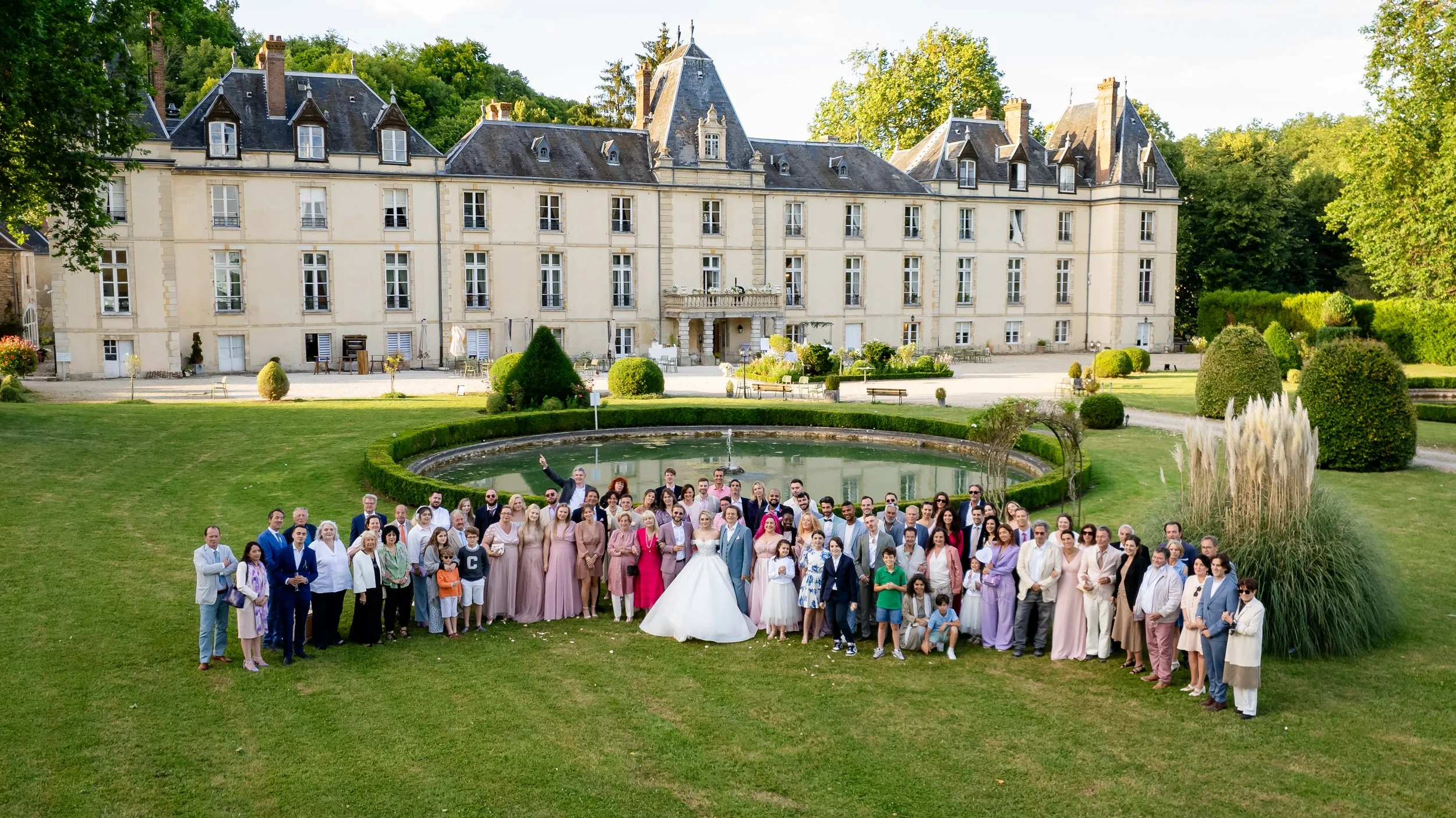 Grande photo de groupe des mariés entourés de leurs invités devant le Château d’Aveny dans le Vexin, lors d’un mariage chic et haut de gamme – photo Stéphane Bourgeon Photography