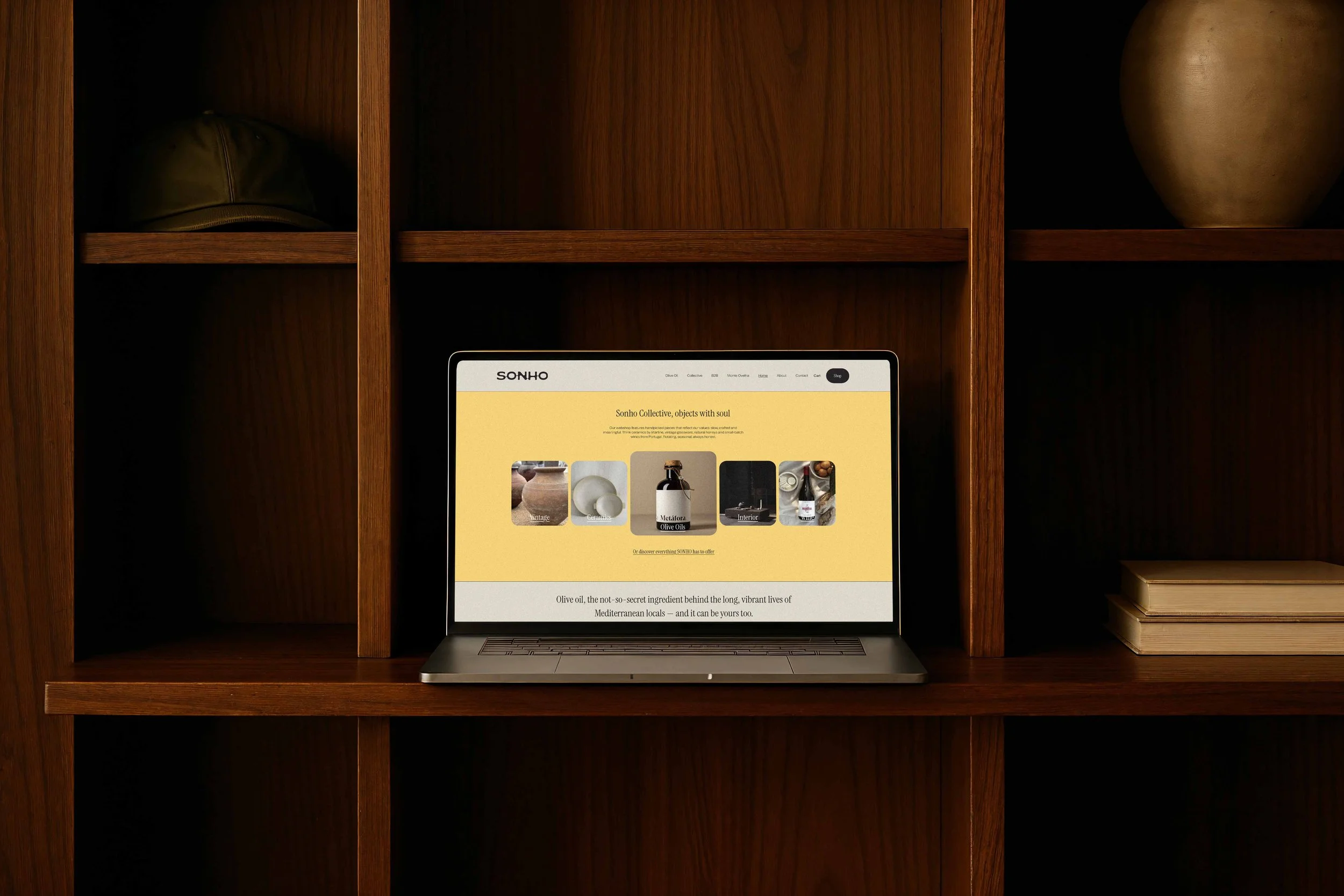 Laptop on a wooden shelf displaying a website with a yellow background and images of pottery, a jar, and labeled products.