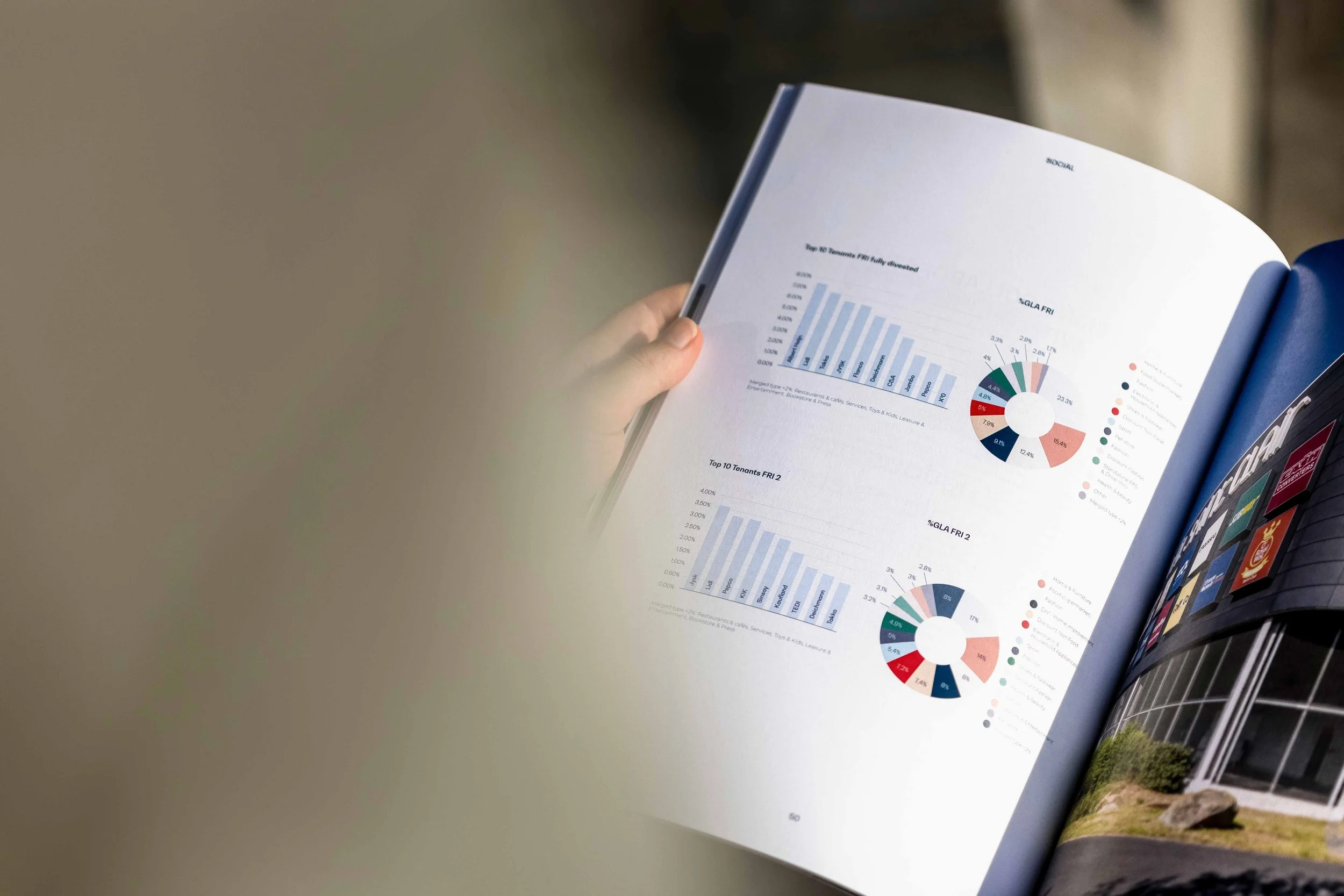 A person holding an open magazine displaying bar graphs and pie charts, with a building visible on the adjacent page.