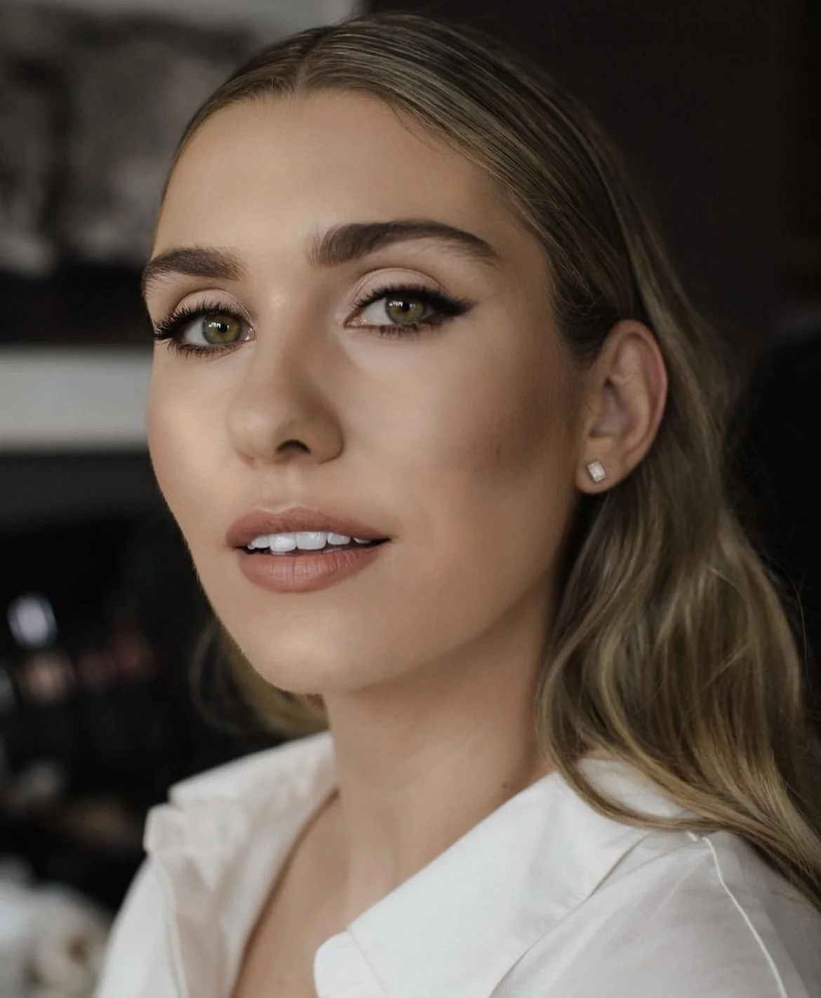 Close-up of a woman with light brown hair, green eyes, makeup, and diamond stud earrings.