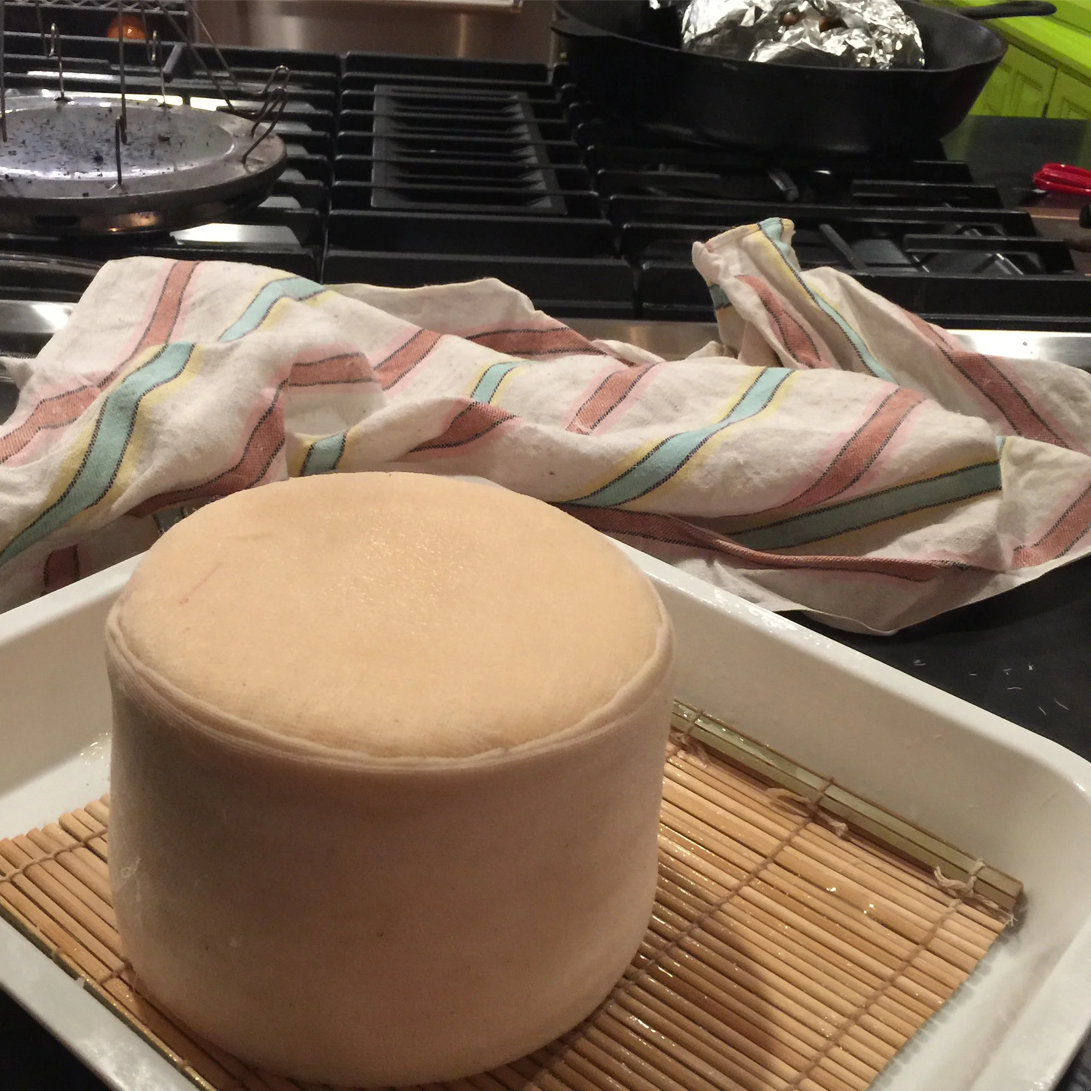 large cloth wrapped cheese on a bamboo mat in a white plastic tray natural cheesemaking