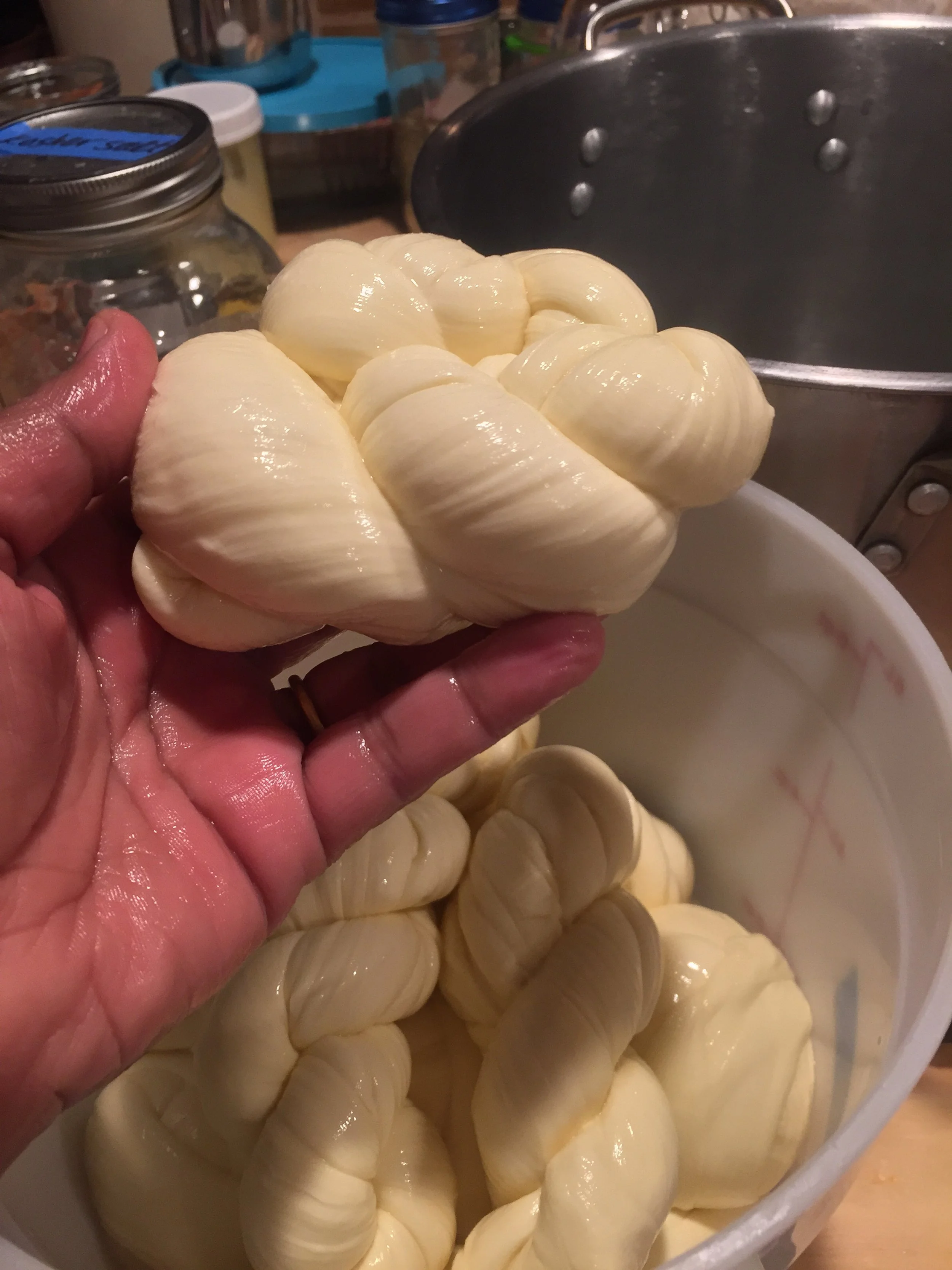 hand holding mozzarella cheese over a bucket filled with mozzarella cheese