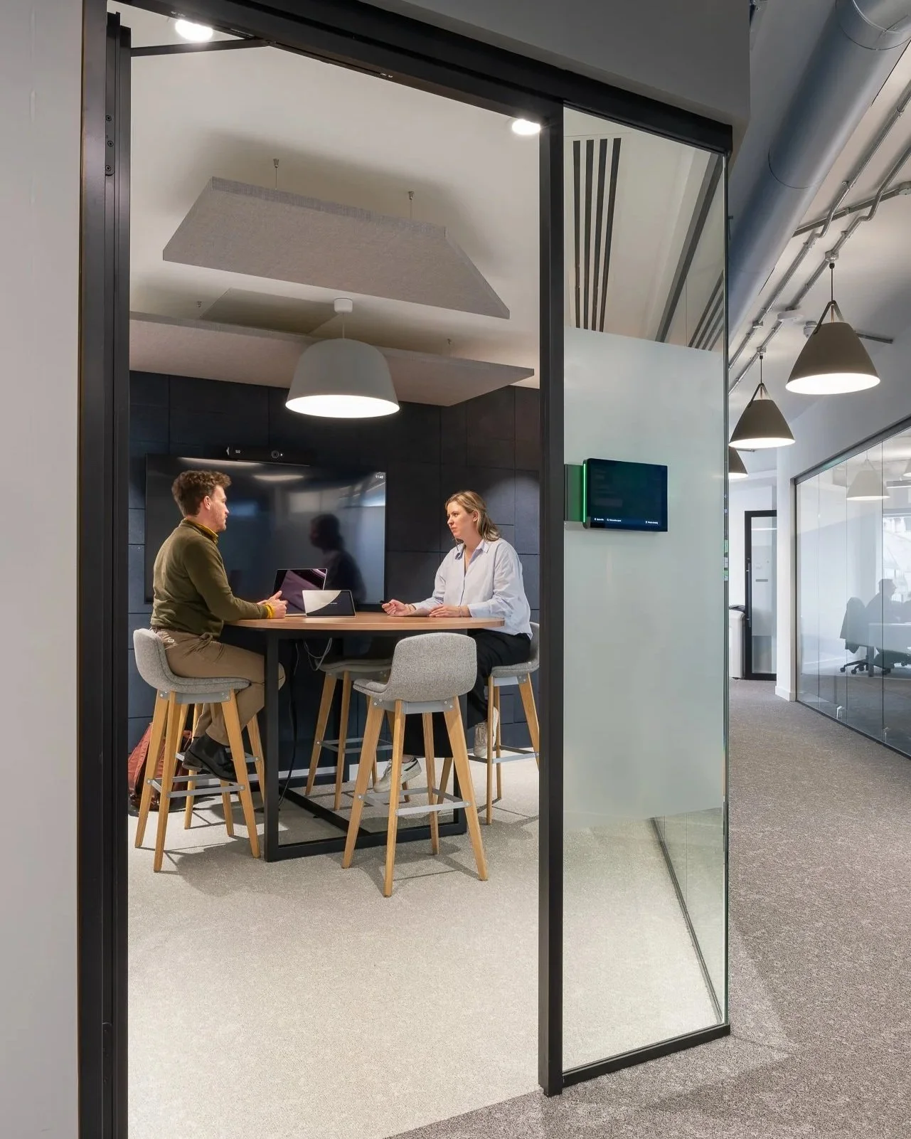 Two people having a discussion in a modern office conference room, seen through a glass door.