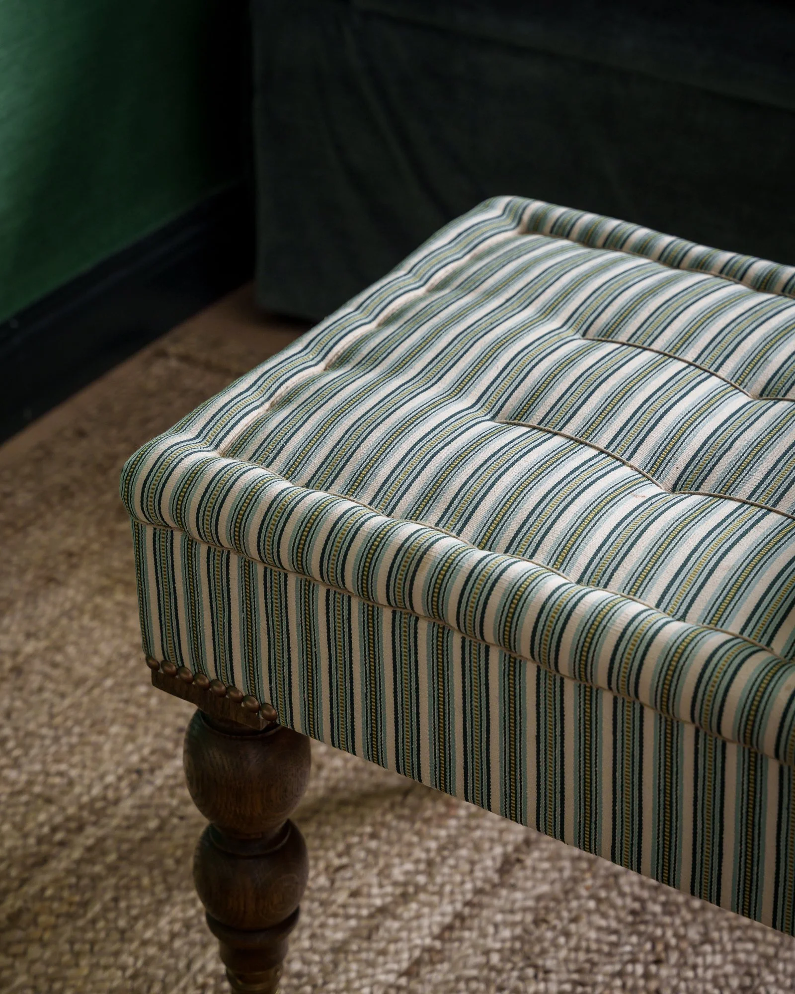 Close-up of a wooden chair with a striped cushioned seat, background shows a green wall and carpeted floor.