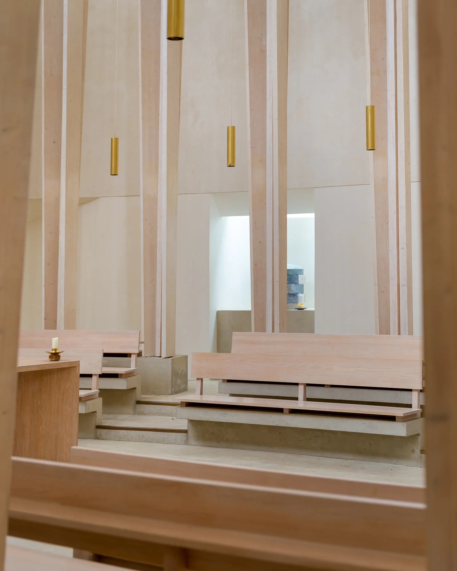 Interior view of a minimalist space with wooden slats, benches, and candle holders. Gold cylindrical hanging lights add to the aesthetic.