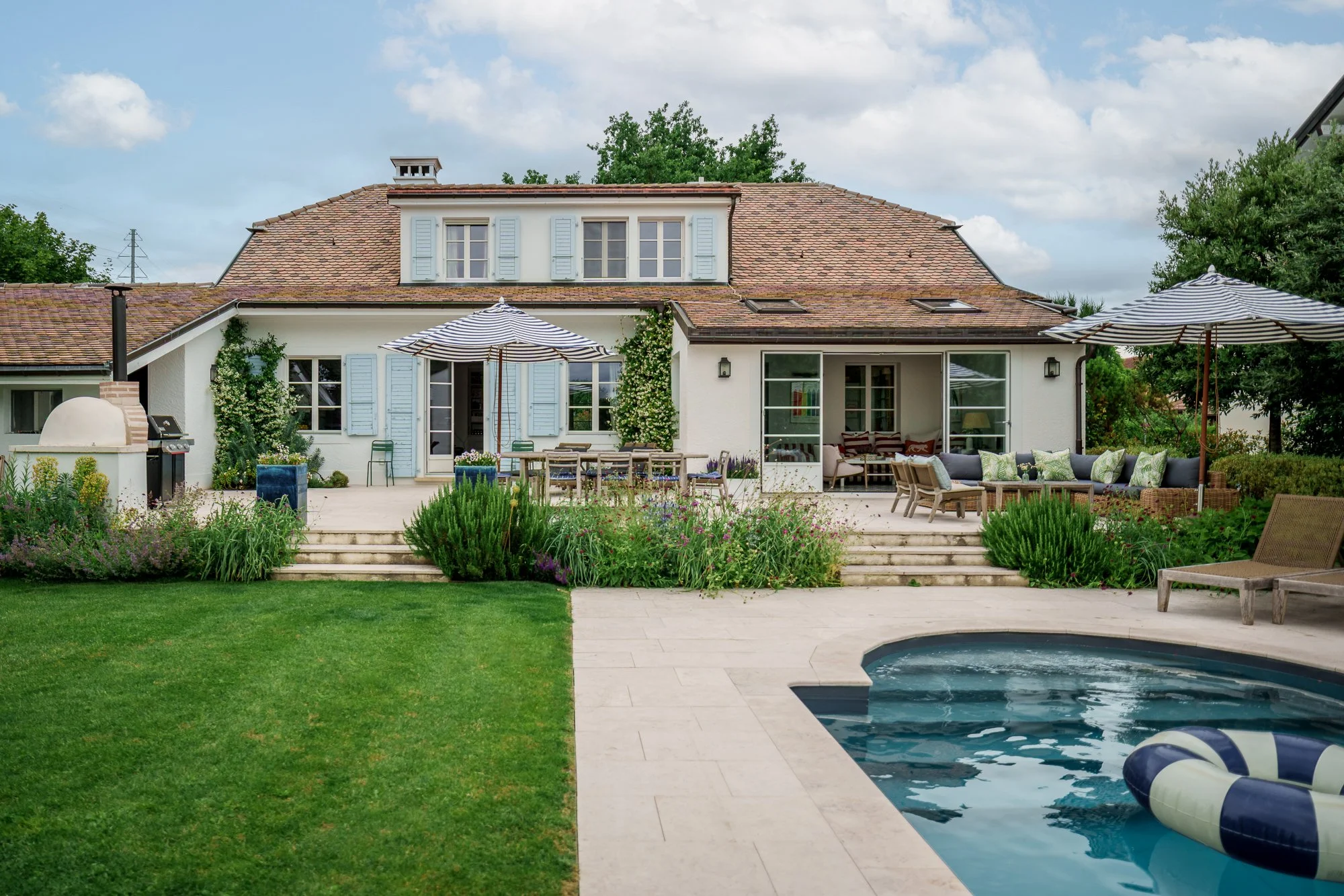 Backyard scene with a house, patio, swimming pool, lounge chairs, and umbrellas
