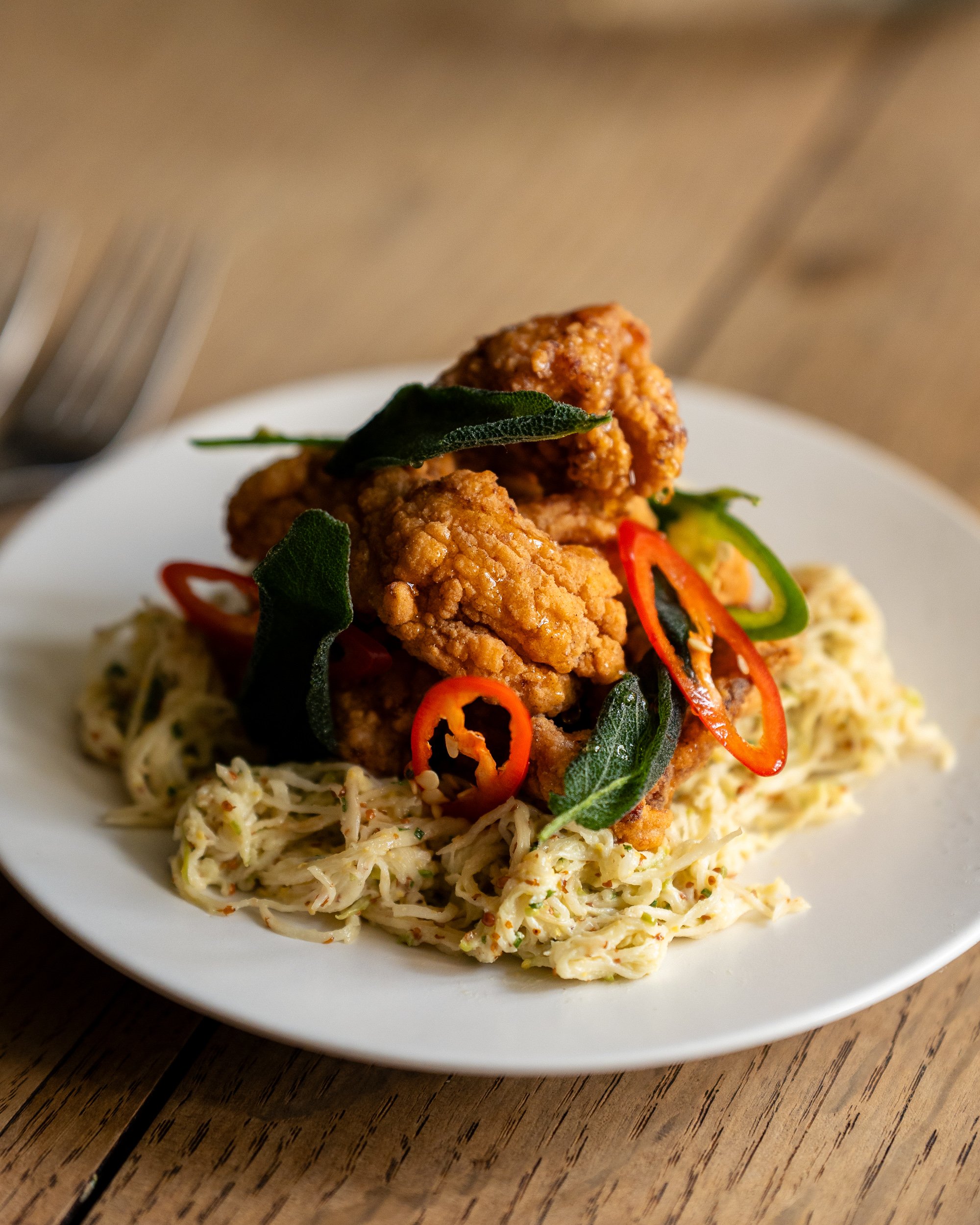 Fried chicken served on a bed of coleslaw with red and green chili peppers and sage leaves on top, on a white plate.
