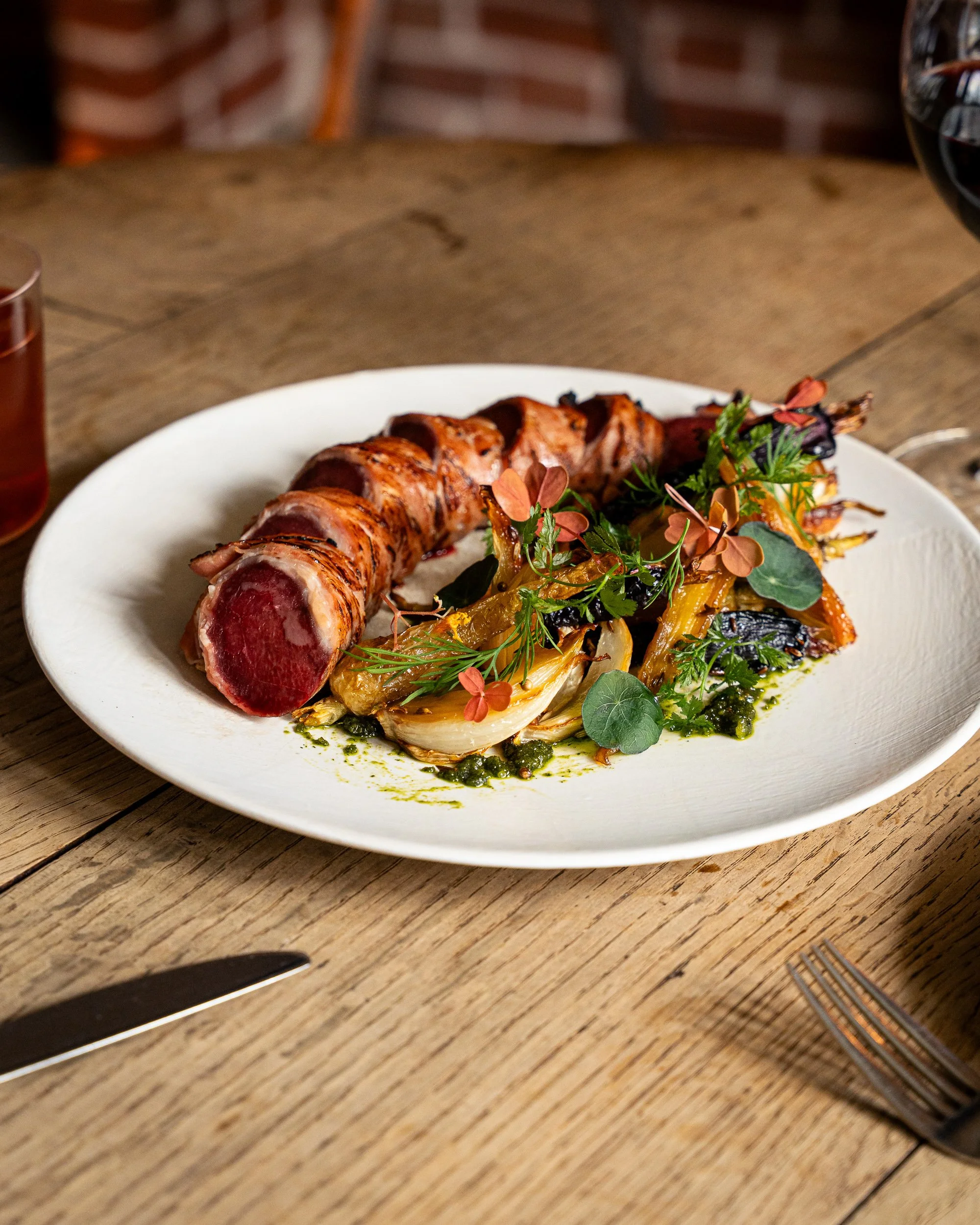 Plate of seared tuna with roasted vegetables and green herbs served on a wooden table.