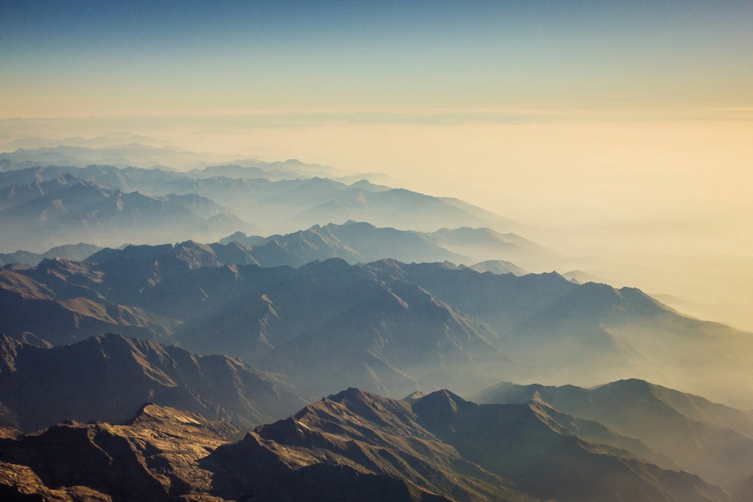 Aerial view of mountain ridges fading into the horizon with a bright, hazy sky.