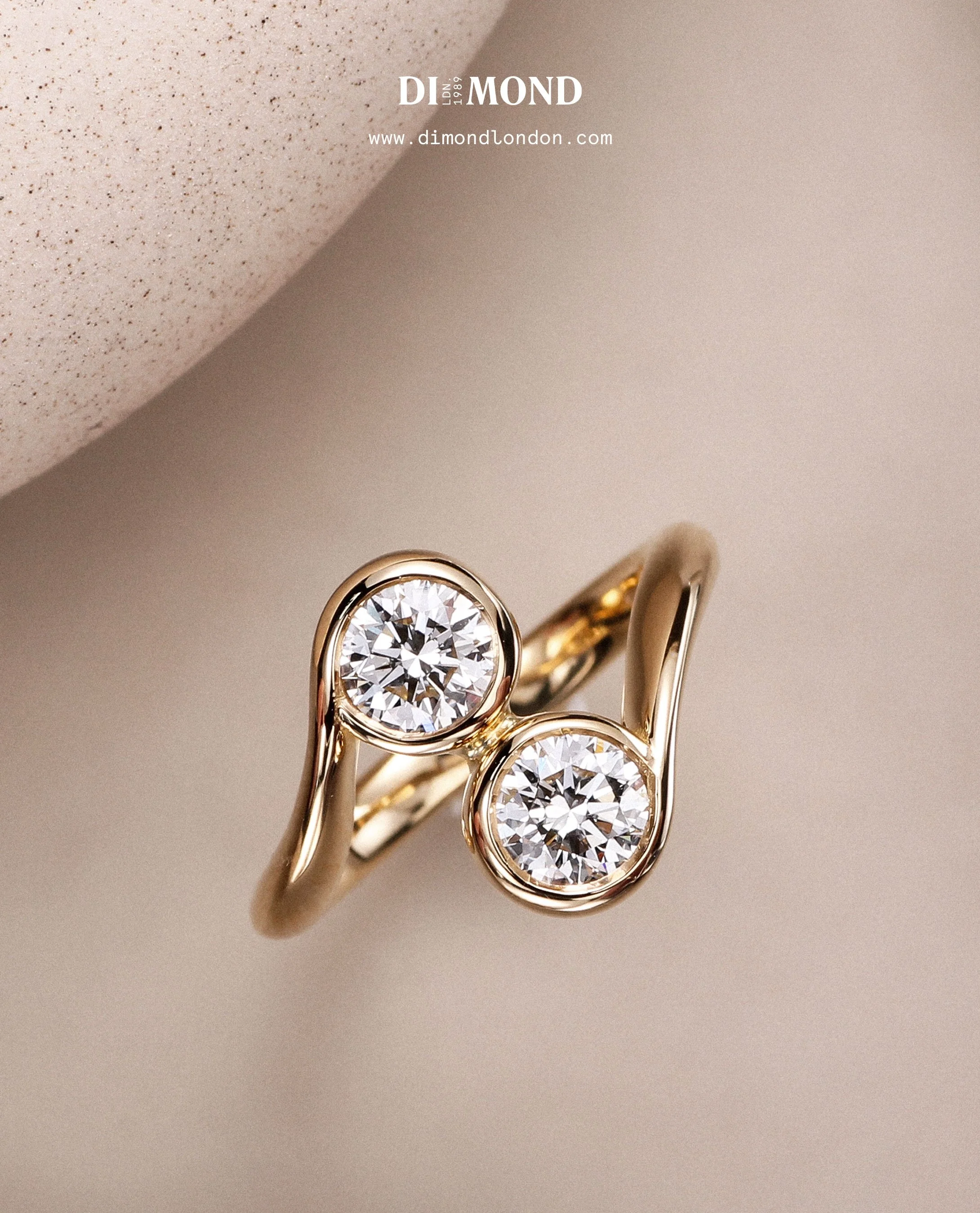 Gold ring with two diamonds against beige background.