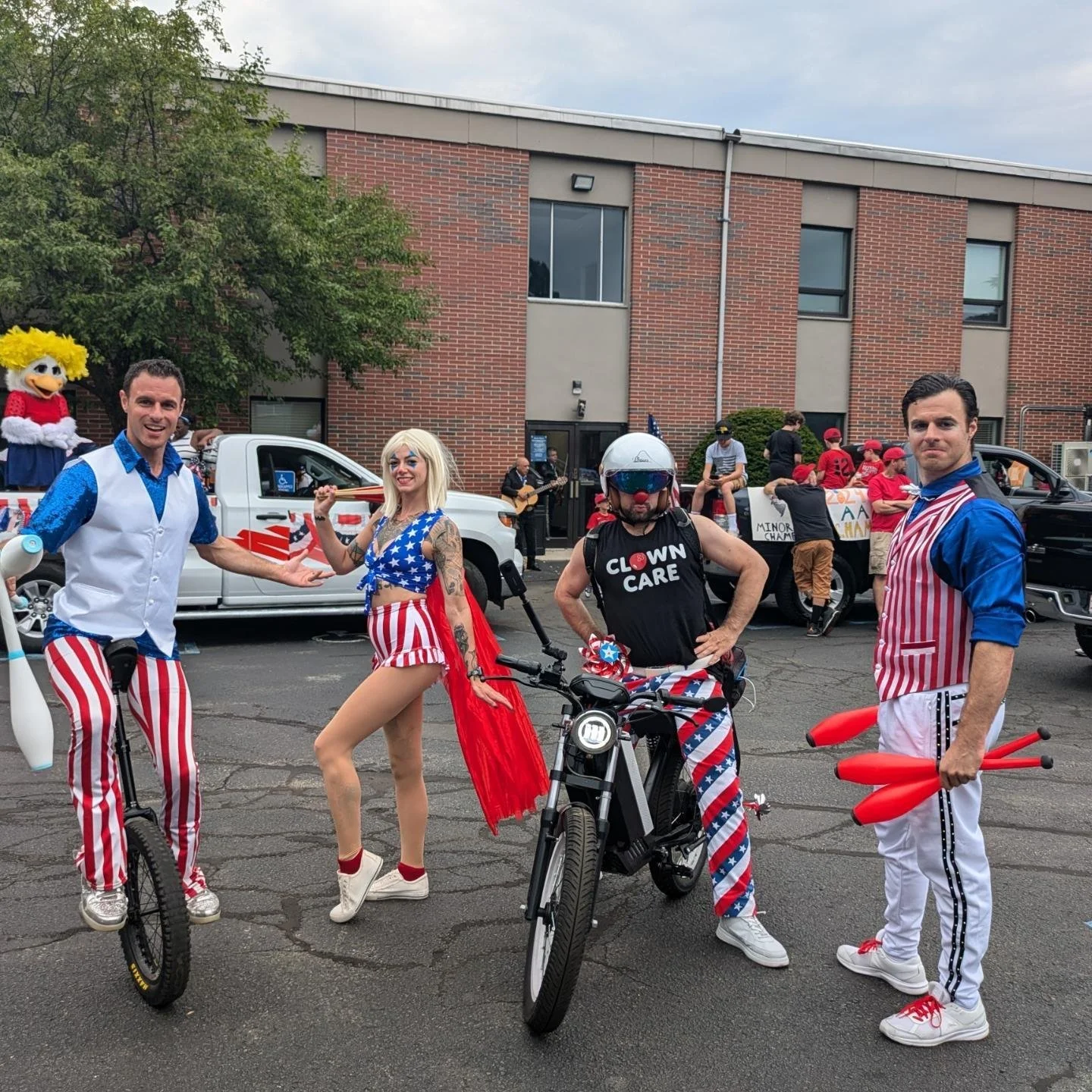 People dressed in patriotic costumes celebrating outdoors, with a float and signs in the background, during a parade or festival.