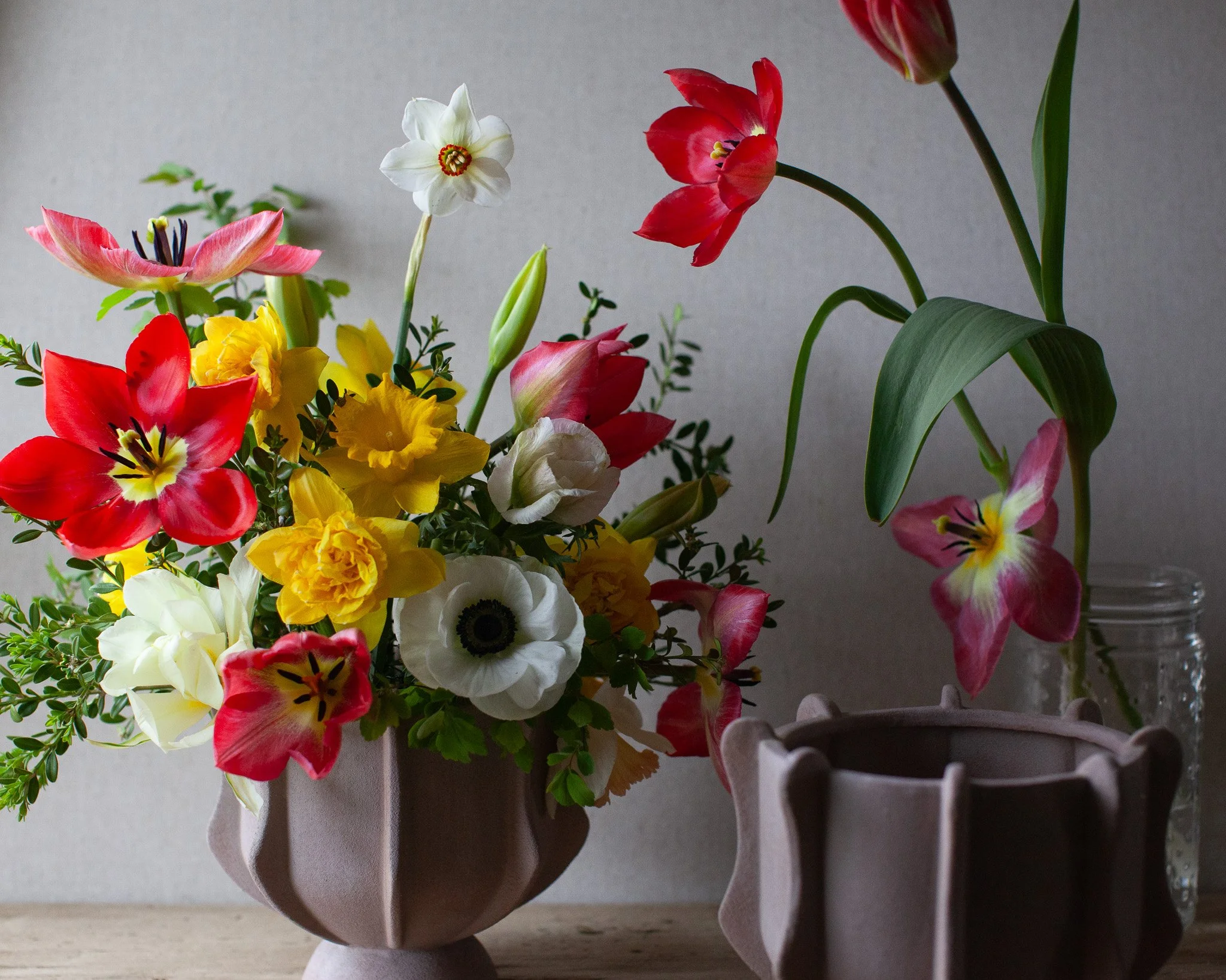 A wooden table with a colorful bouquet of various flowers, a small white bowl, and two round objects that appear to be flower arrangements or decorations.