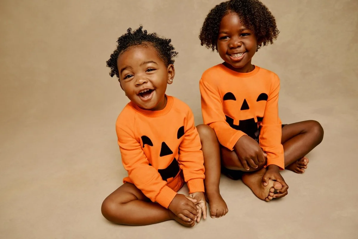 Two model siblings in matching pumpkin outfits from Little Sleepies. 