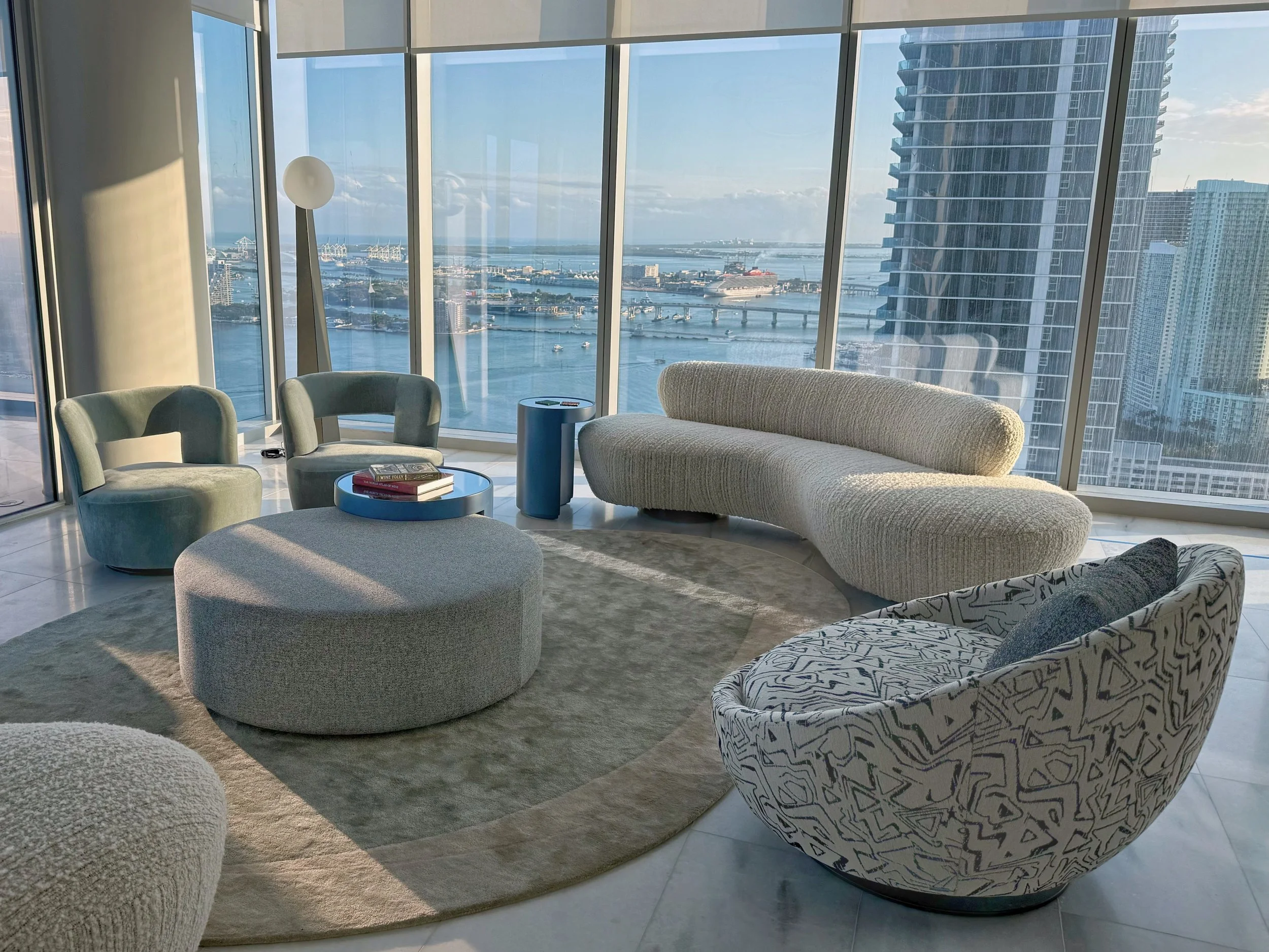 Designed for elevated coastal living, a modern penthouse interior such as in Sunny Isles Beach, Miami features large floor-to-ceiling windows that showcase stunning ocean and skyline vistas. A curated arrangement of curved modern sofas, textured fabr