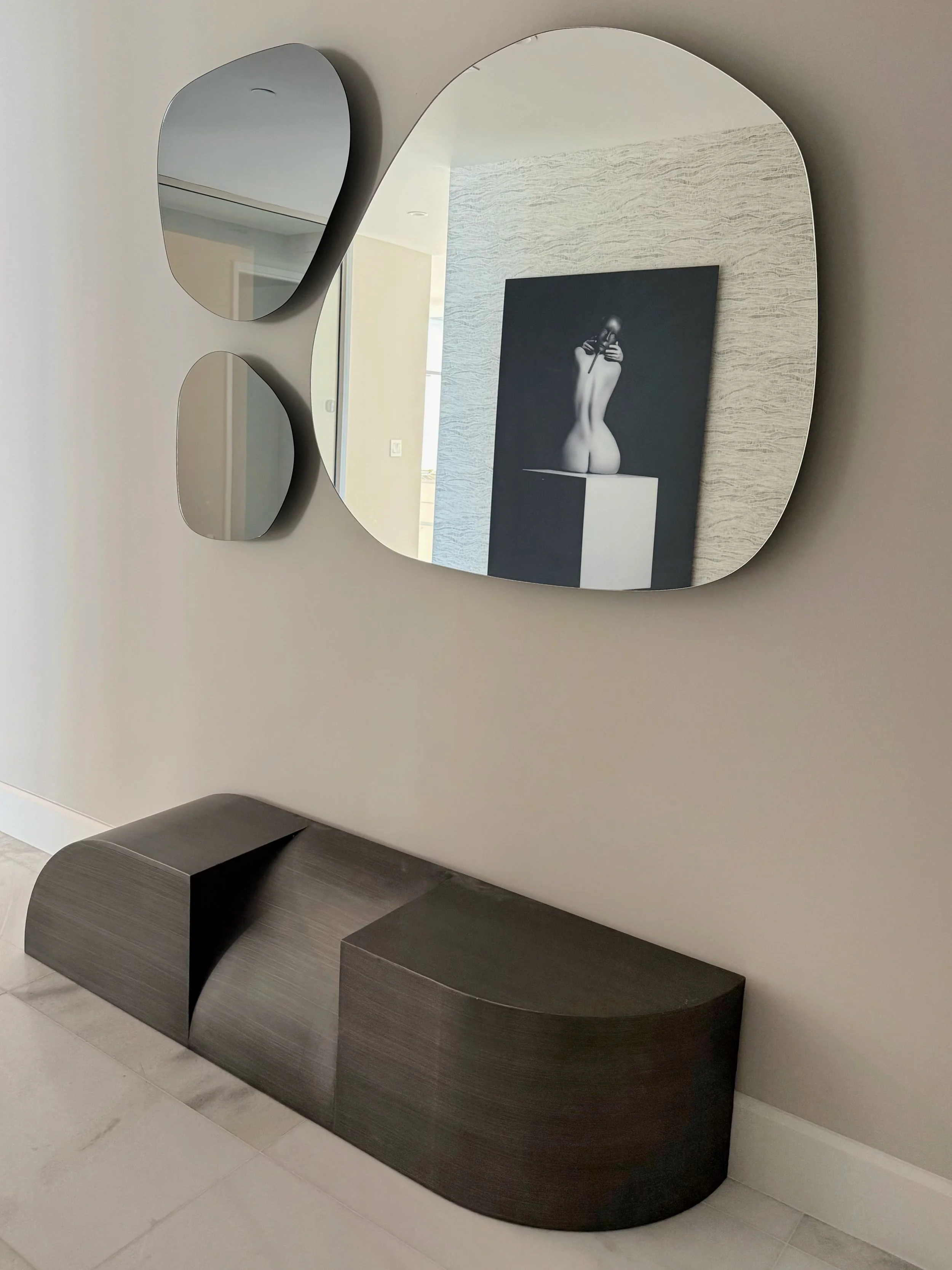 A sophisticated grand foyer in a luxury Edgewater Miami penthouse condo introduces a refined modern interior design aesthetic with curated architectural details and sculptural furnishings. A geometric contemporary bench in dark metallic finish anchor