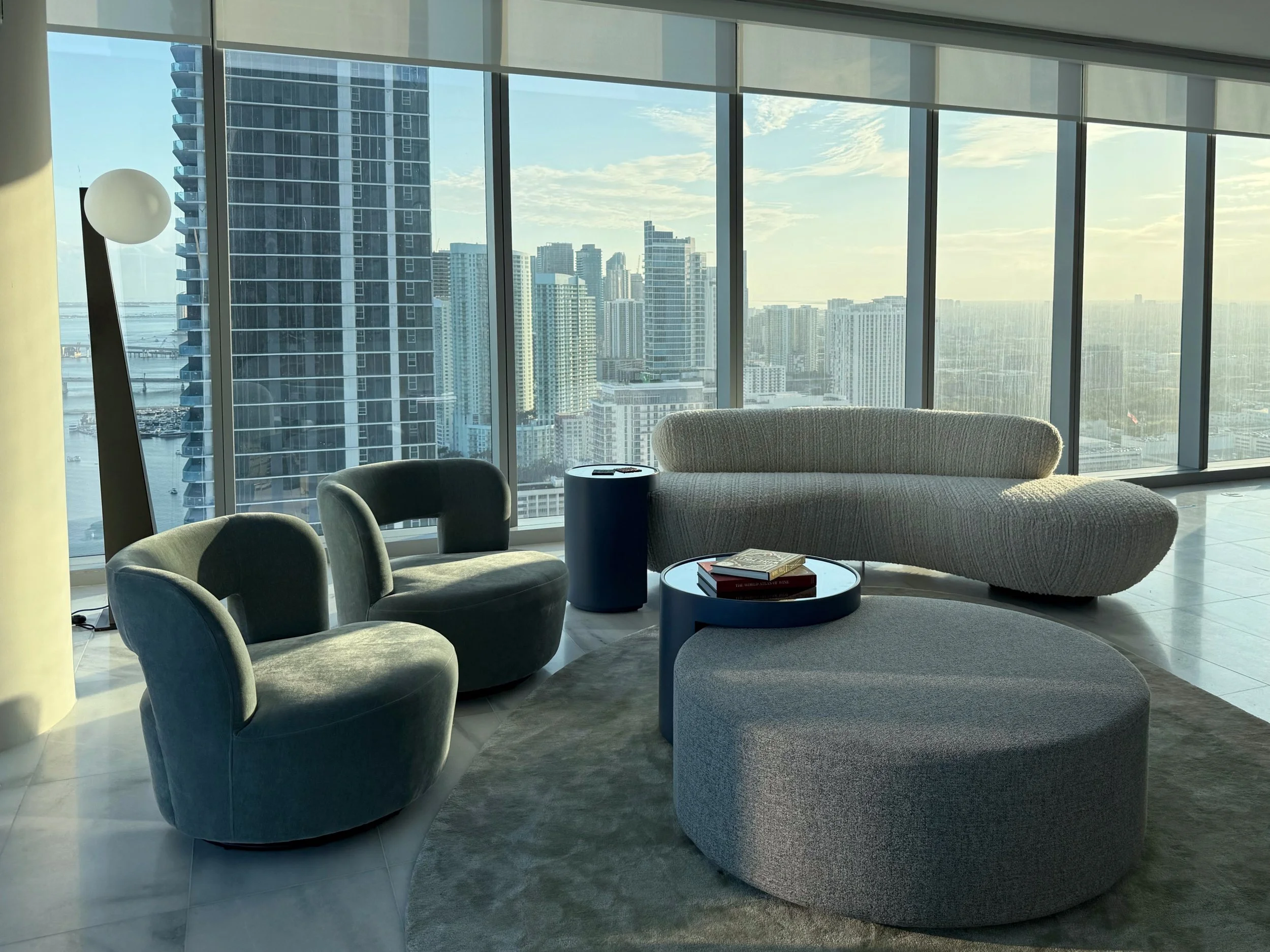 Located in the exclusive South of Fifth neighborhood of Miami Beach, a contemporary penthouse living room highlights modern minimalist interior design with expansive windows capturing breathtaking coastal and skyline views. Sculptural furniture with 