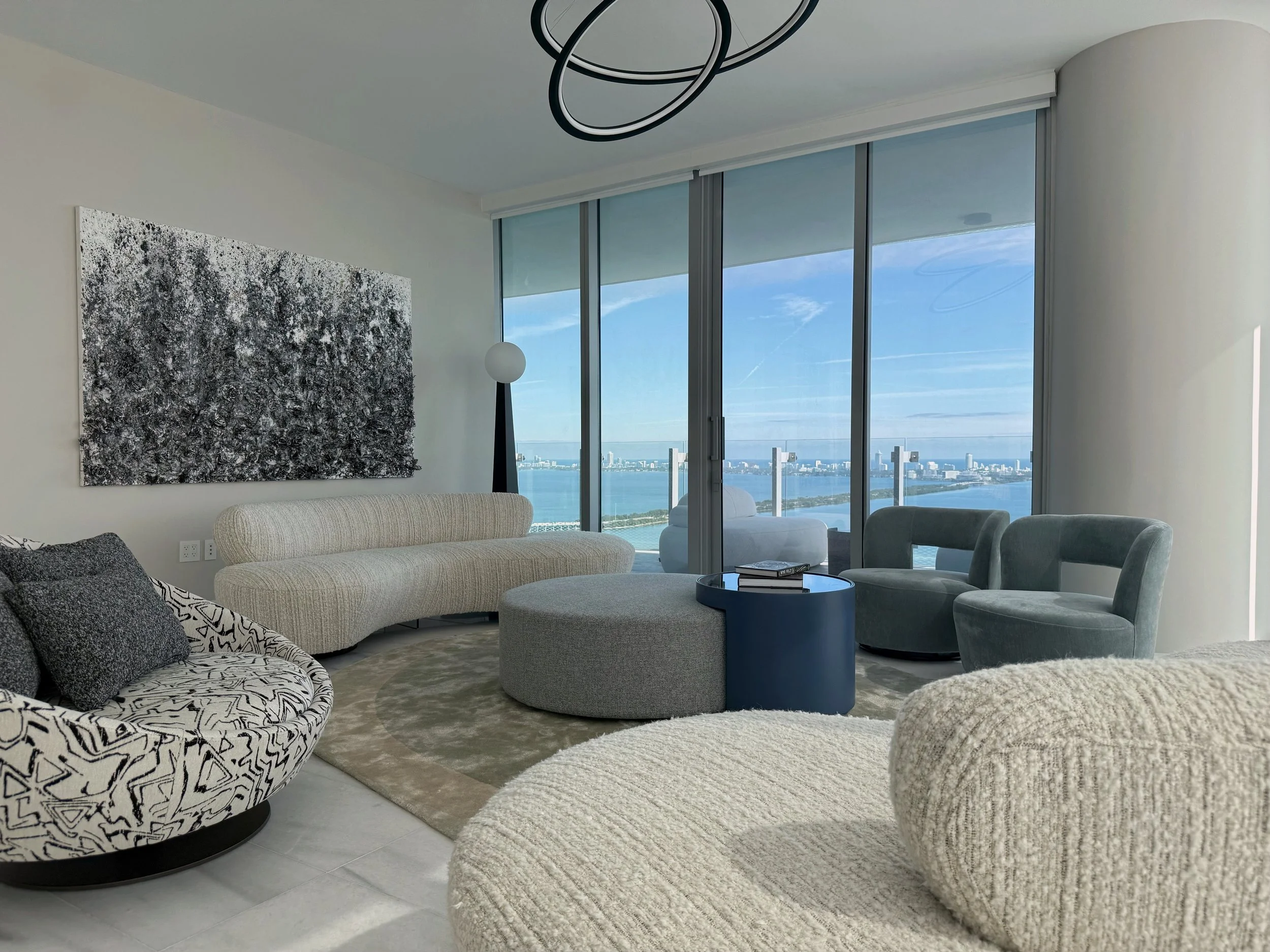 Sophisticated penthouse living room such as in Bal Harbour, Miami blends contemporary interior design with breathtaking panoramic views through expansive glass windows. Sculptural seating upholstered in luxurious boucle fabric defines the conversatio