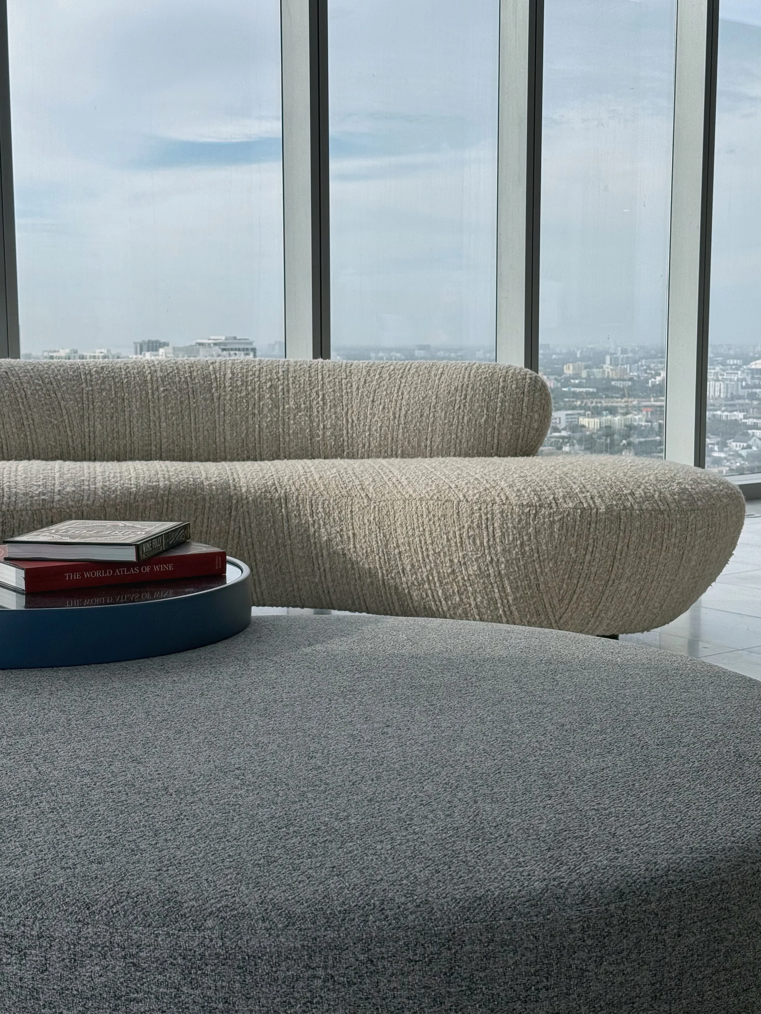 Elegant penthouse living space such as in Brickell, Miami highlights modern condo interior design with expansive glass walls capturing panoramic views of Biscayne Bay and the downtown skyline. Soft boucle sofas with sculptural silhouettes anchor the 