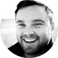 Black-and-white portrait of a smiling person with short hair and a beard.