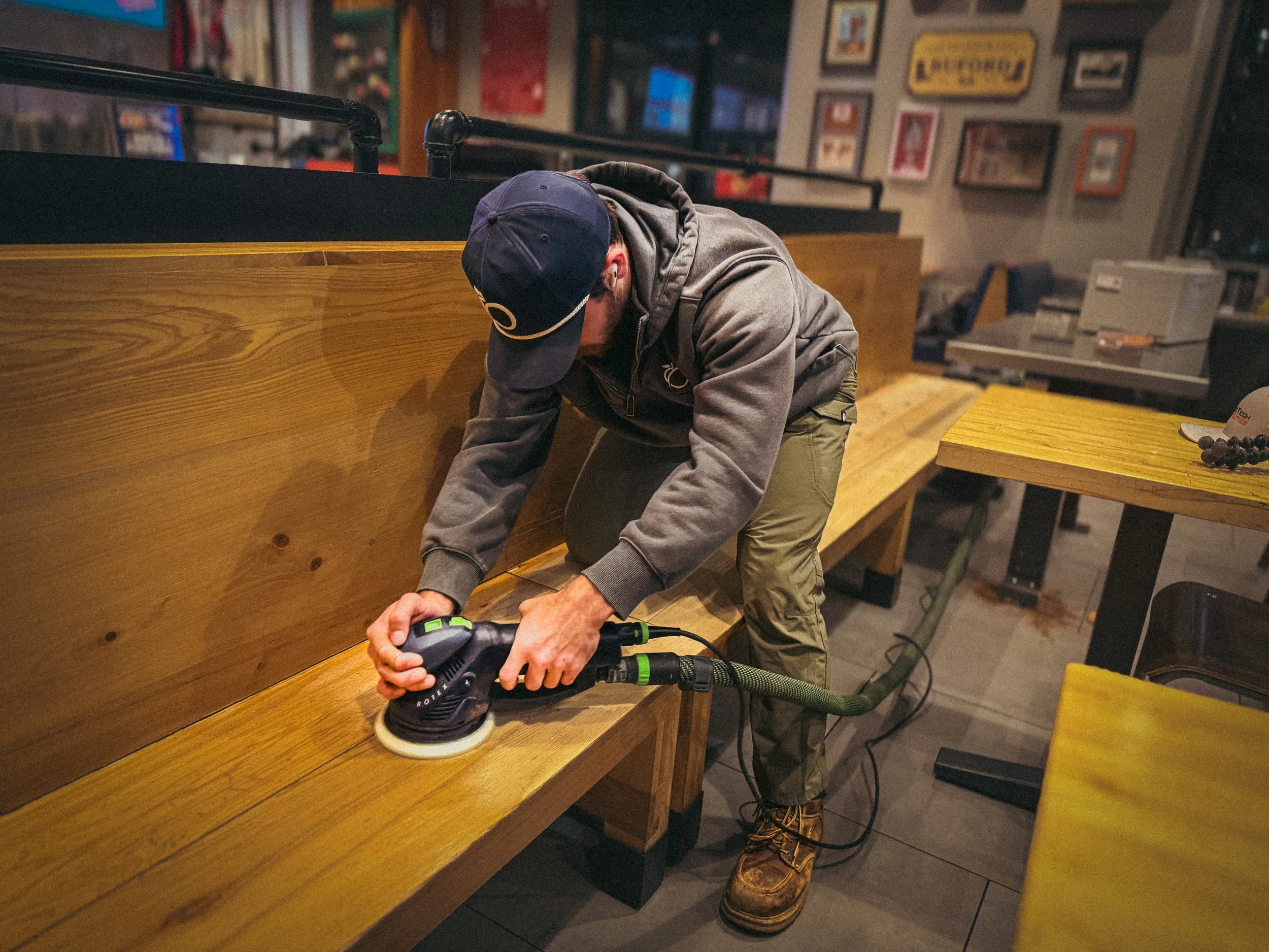 Handyman with a festool rotex in hand sanding a commercial quick service restaurant wooden bench