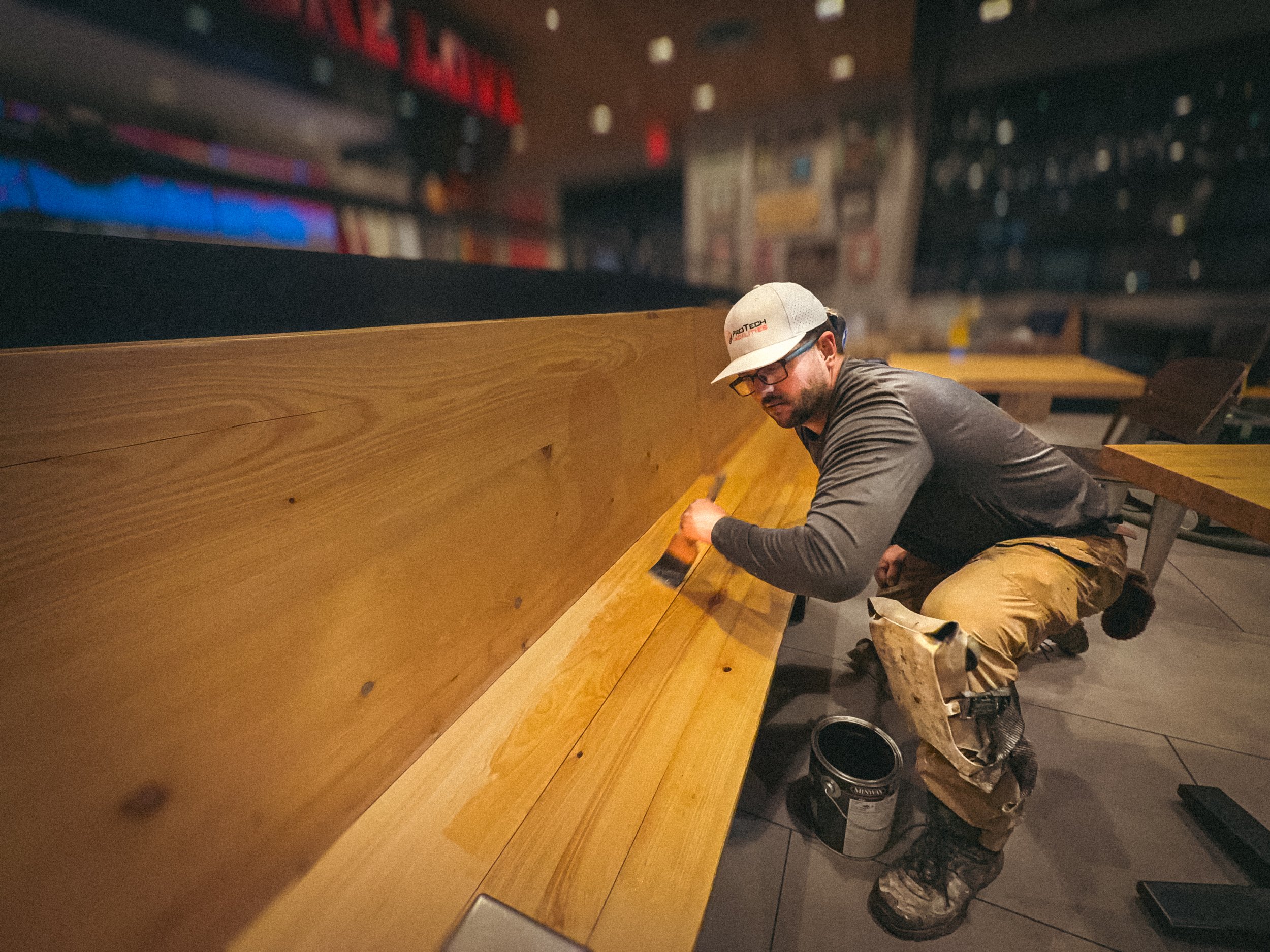 Commercial handyman applying a coat of oil based polyurethane to a quick service restaurant wooden bench in Buford, GA