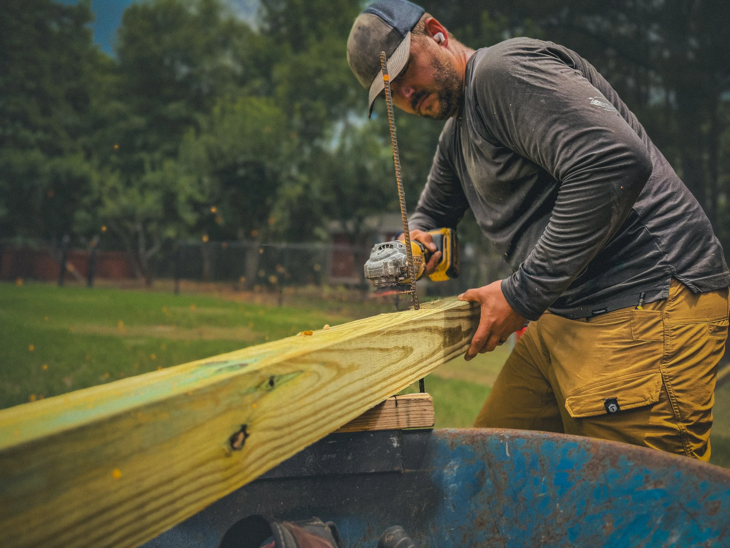 Carpenter using an angle grinder to cut rebar that is inserted into a fence post for a fence repair project in Watkinsville, GA