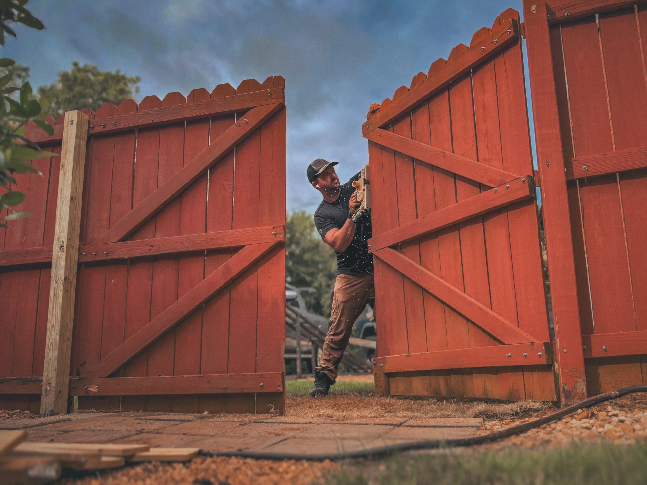 Carpenter using a power plane between two gate fences adjusting the gate for a fence repair job in Watkinsville, GA